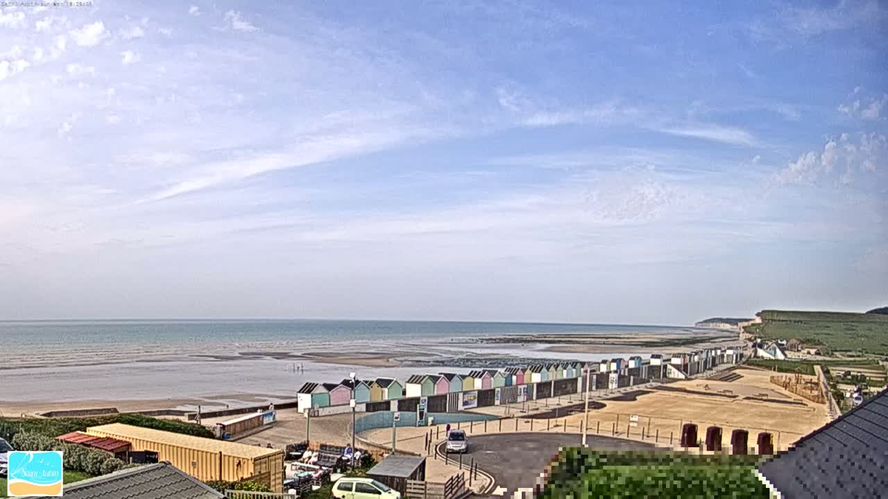 A row of colorful beach huts lines a sandy beach, overlooking a calm sea under a mostly clear, bright sky.