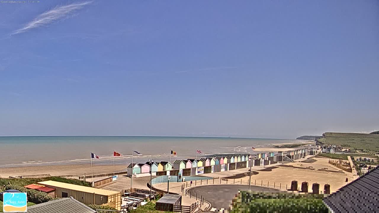 A row of colorful beach huts sits on a sandy beach overlooking a calm ocean under a mostly clear sky.
