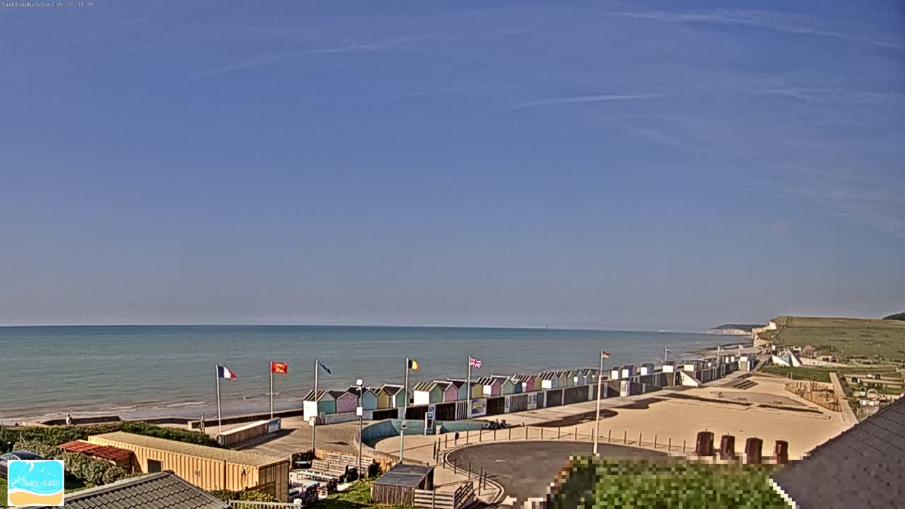 A row of colorful beach huts sits on a sandy beach next to a calm ocean under a clear blue sky.