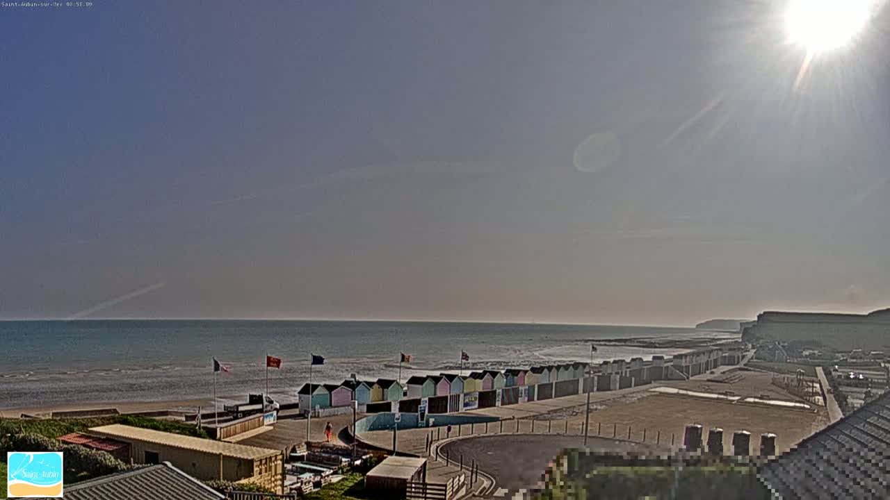 A sunny day at a beach with colorful beach huts lining the shore, a calm ocean, and white cliffs in the distance.