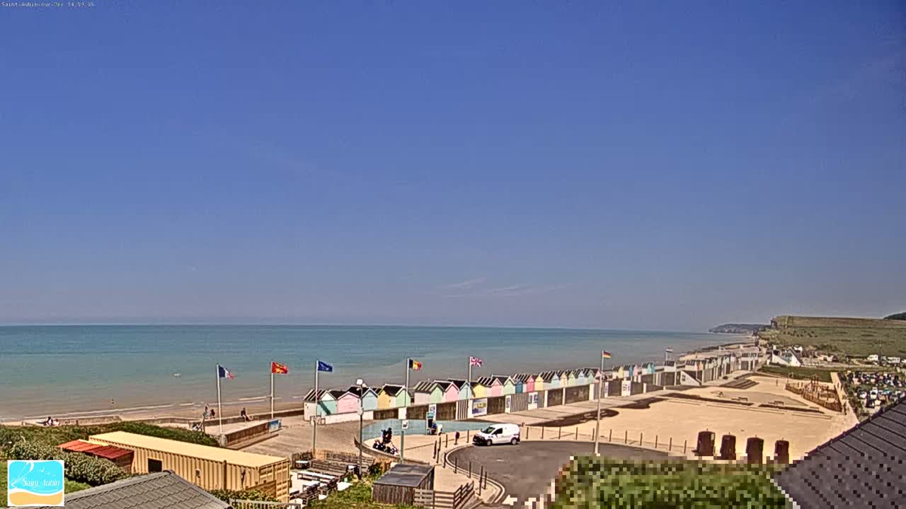 A row of colorful beach huts sits on a sandy beach overlooking a calm ocean under a clear blue sky.