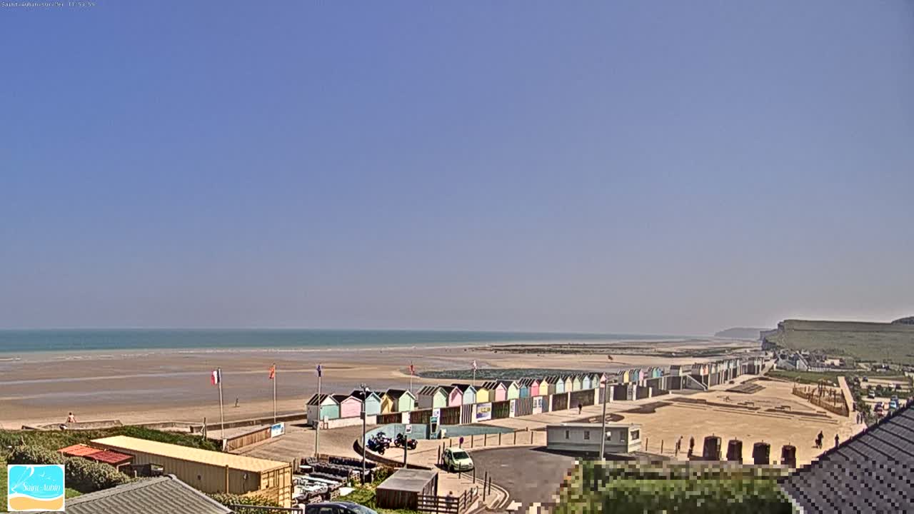 A sandy beach with colorful beach huts stretches along a calm ocean under a clear blue sky.