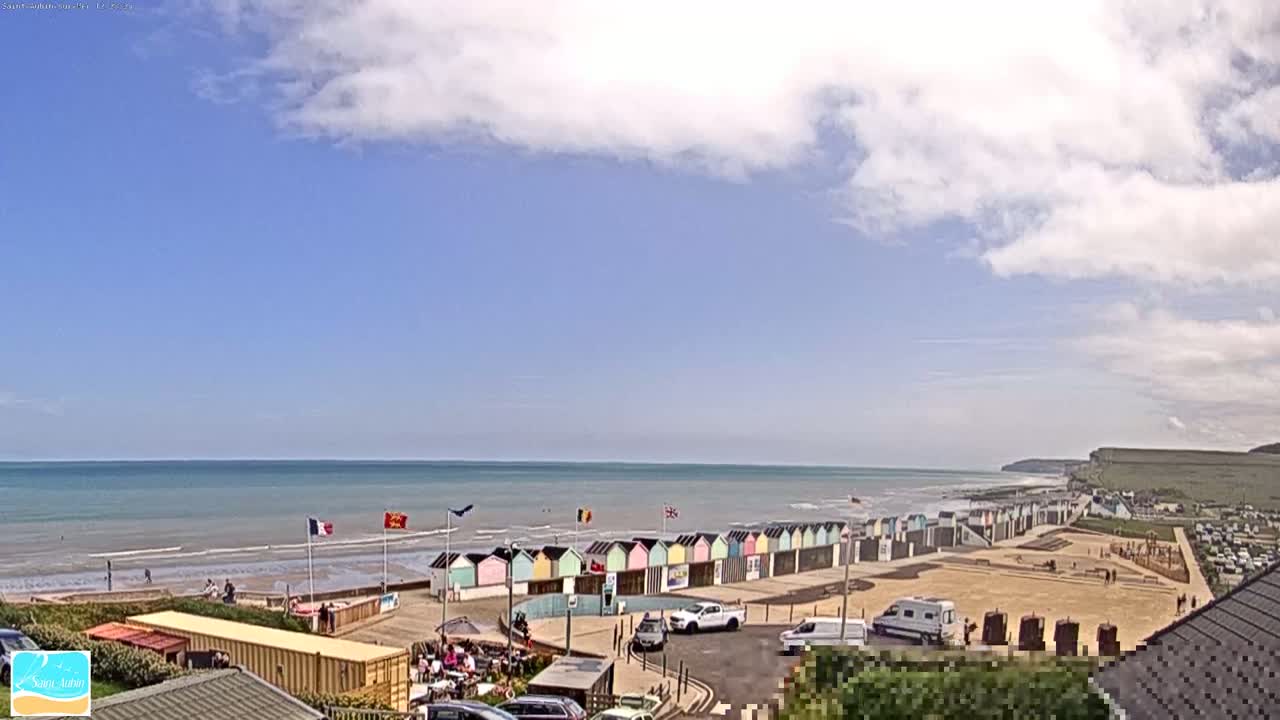 A mostly sunny day at a beach with a row of colorful beach huts, a calm ocean, and white cliffs in the distance.