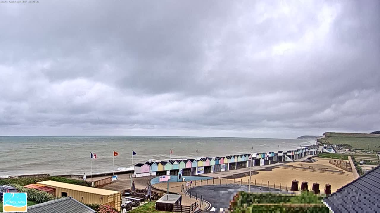 A row of colorful beach huts sits on a sandy beach overlooking a choppy sea under a cloudy sky.
