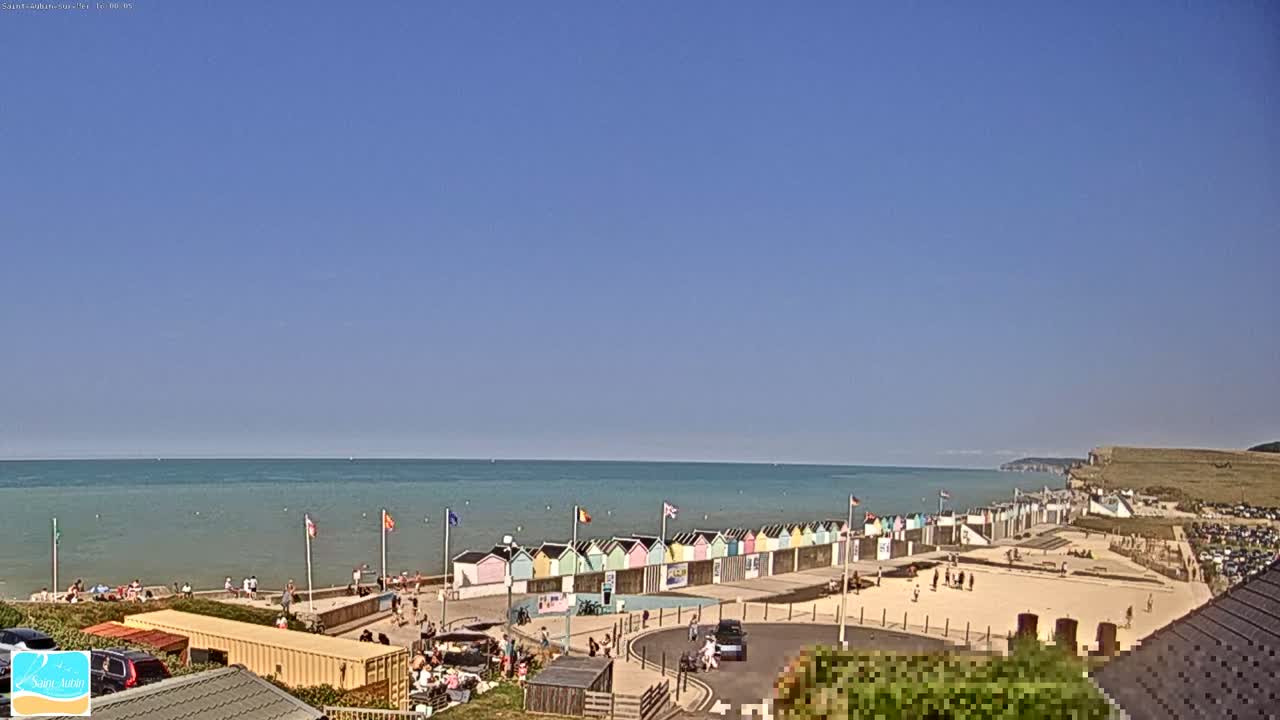 A mostly cloudy day reveals a beach with colorful beach huts, a calm sea, and white cliffs in the distance.