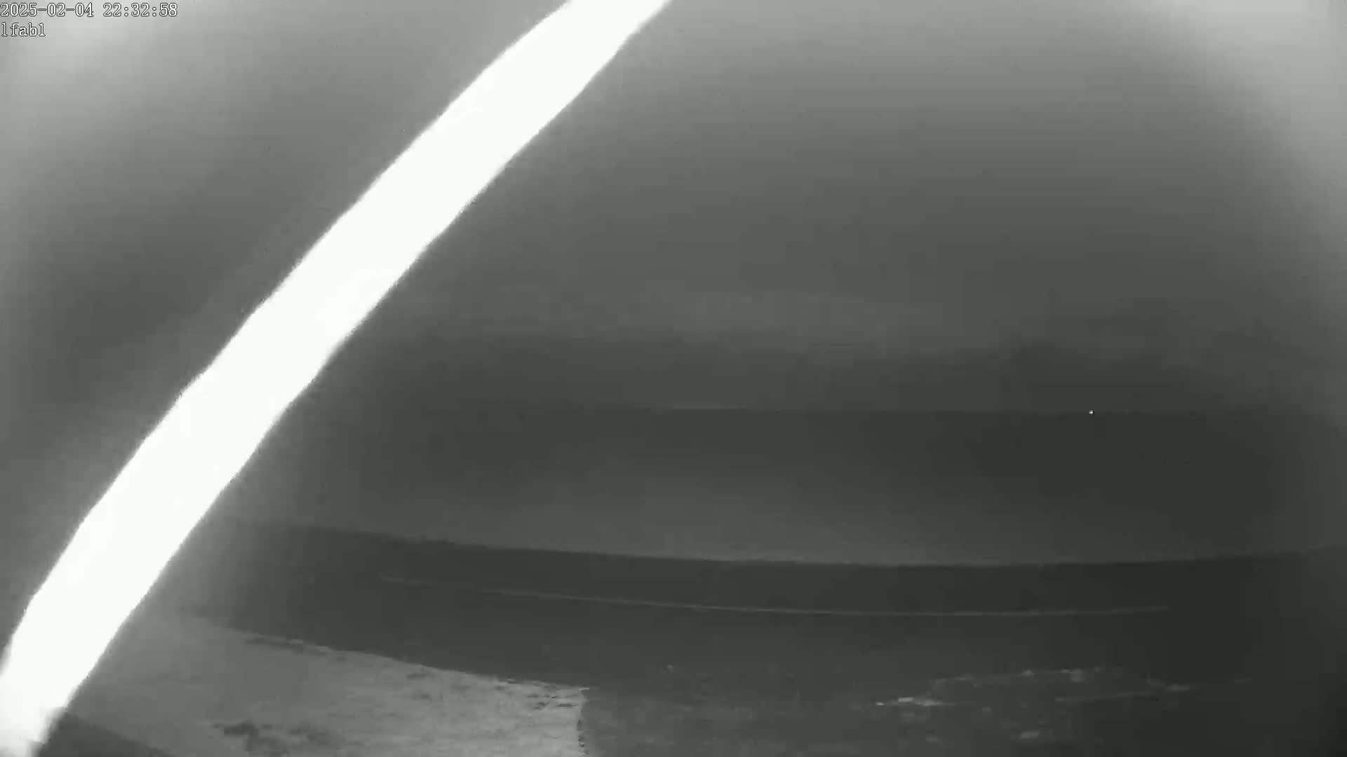 A bright light streaks diagonally across a dark, nighttime sky above a dark body of water.