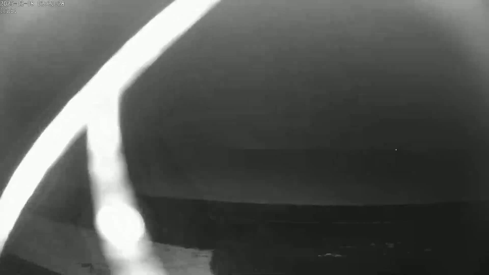 A bright, blurry light streaks across a dark, nighttime sky above a dark, indistinct landscape.
