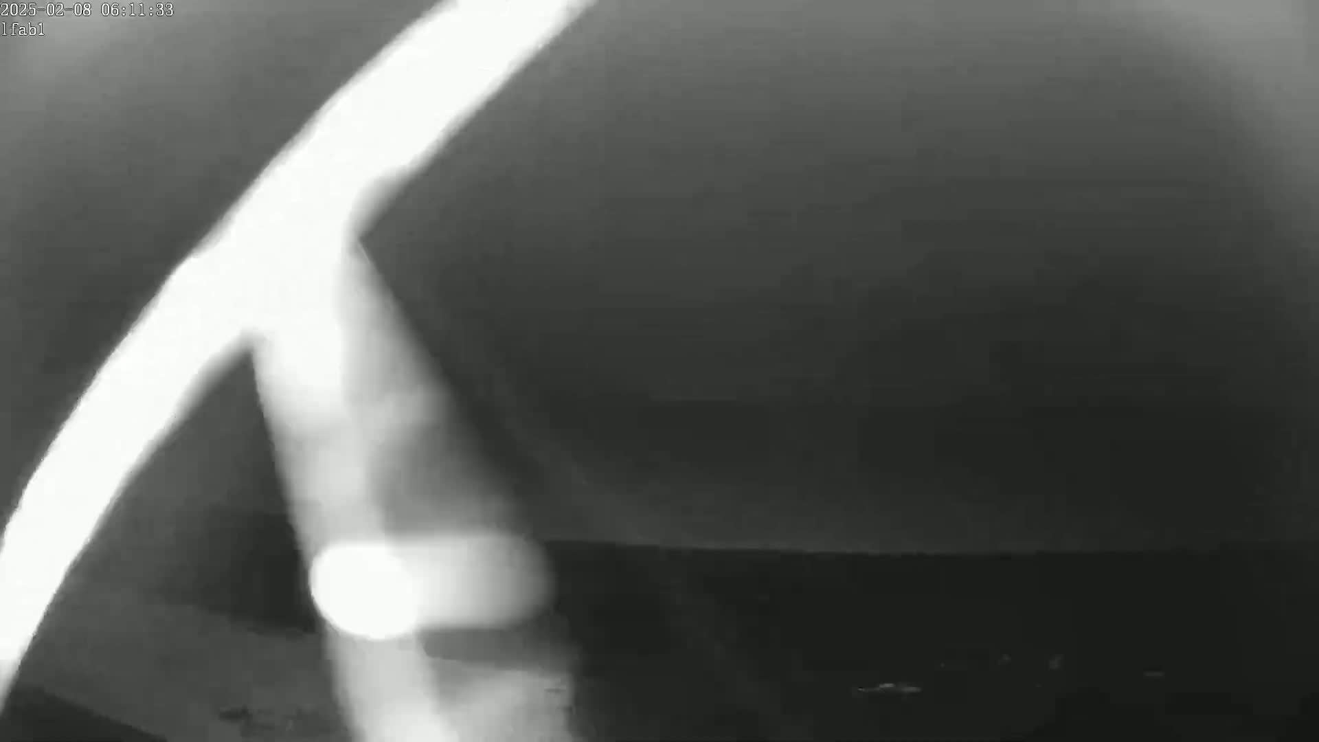 A blurry, grayscale image shows a bright, curved light source in the foreground against a dark, overcast sky.
