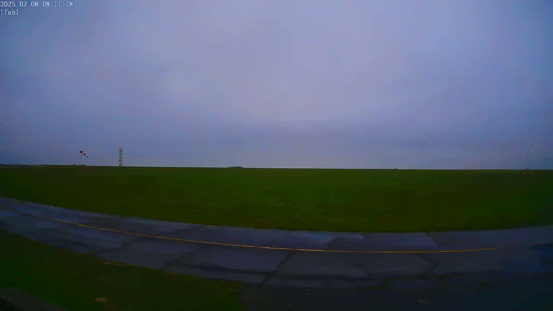 A flat, grassy field with a paved road curving through it under an overcast sky.