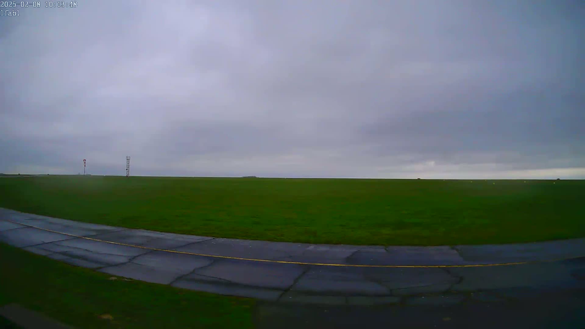 A large expanse of green grass, under an overcast sky, is seen from a low angle, showing a portion of a paved road or runway curving through the foreground.
