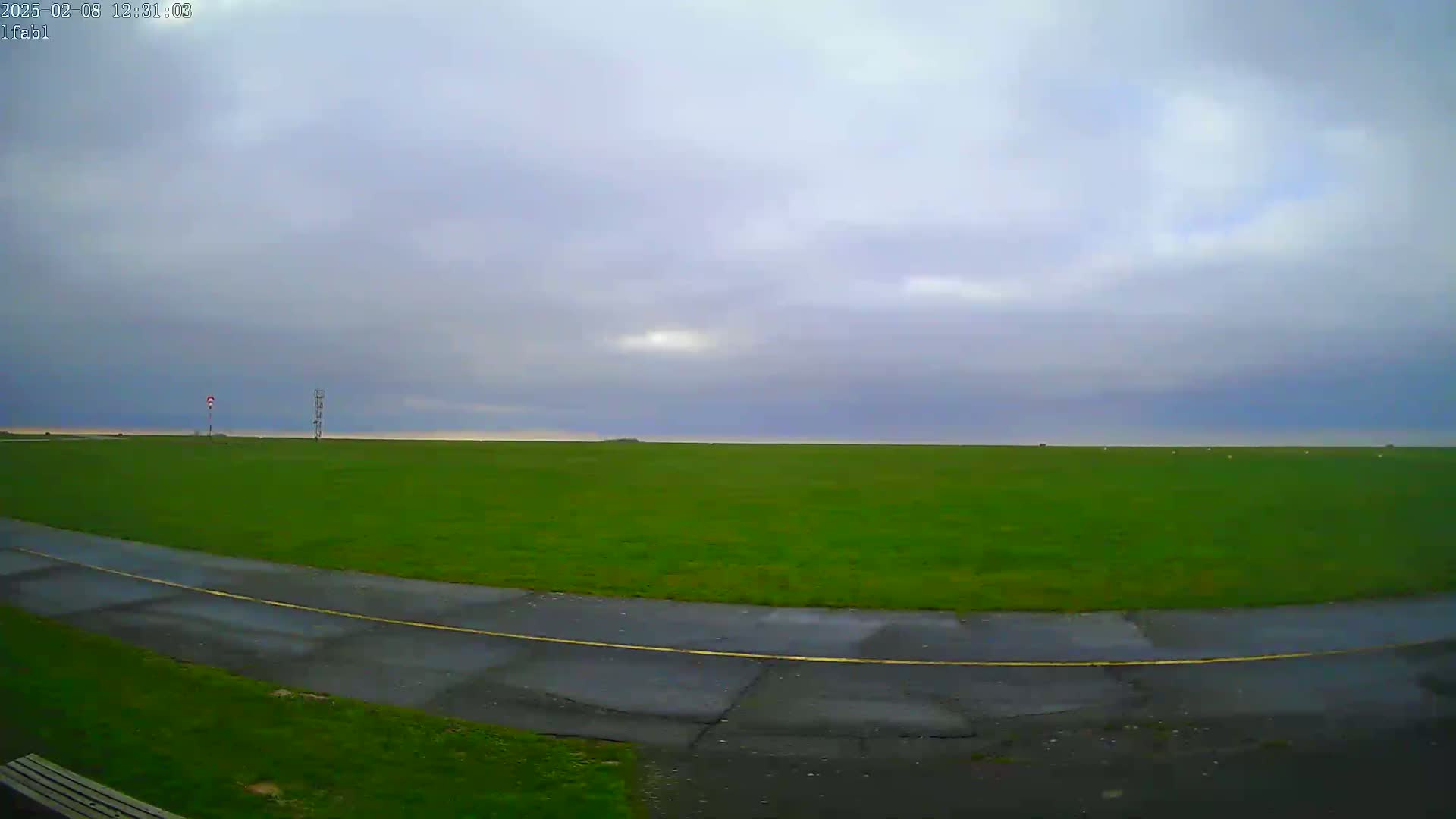 A wide, grassy field under an overcast sky is bordered by a curved asphalt road.
