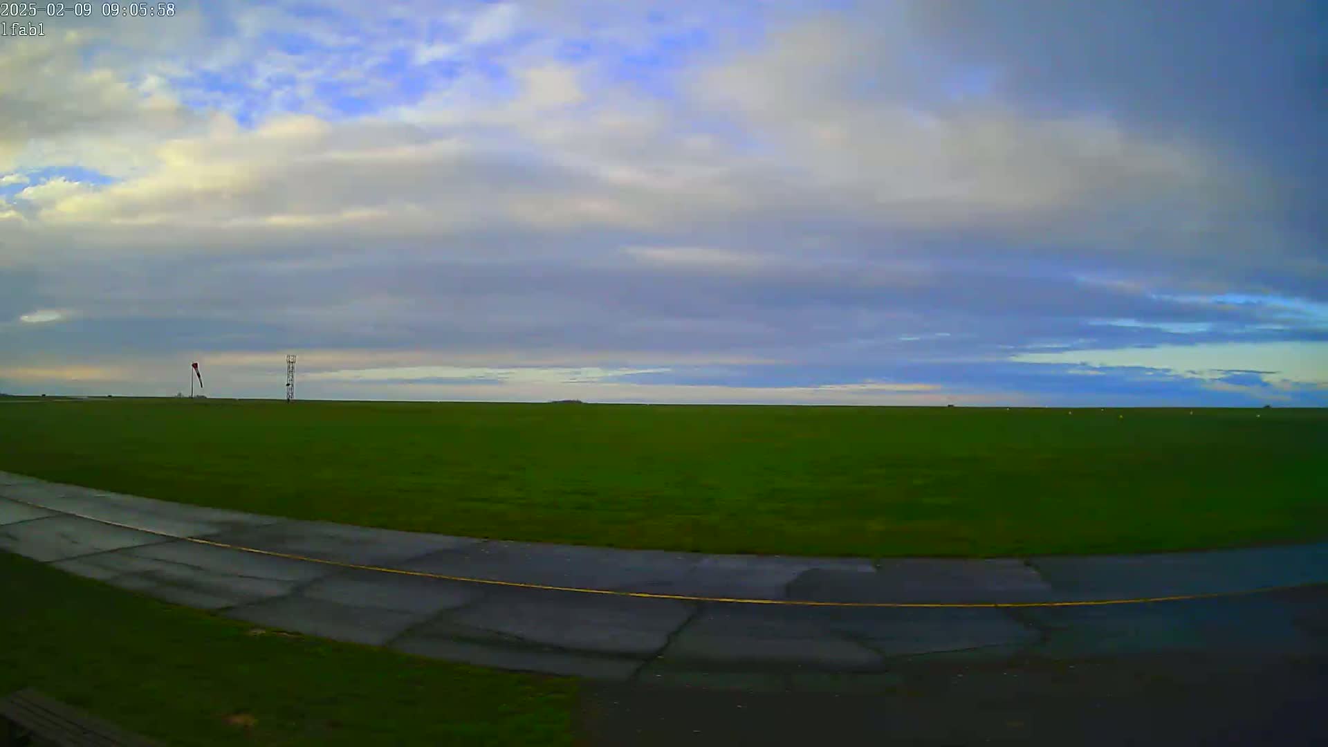 A paved road curves through a grassy field under a mostly cloudy sky.
