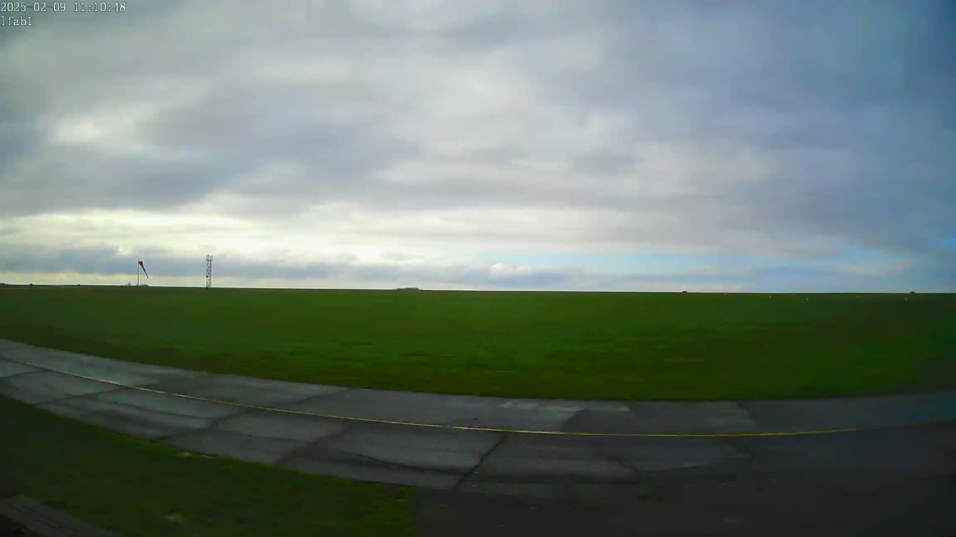A grassy field with a paved road curves into the foreground under an overcast sky.