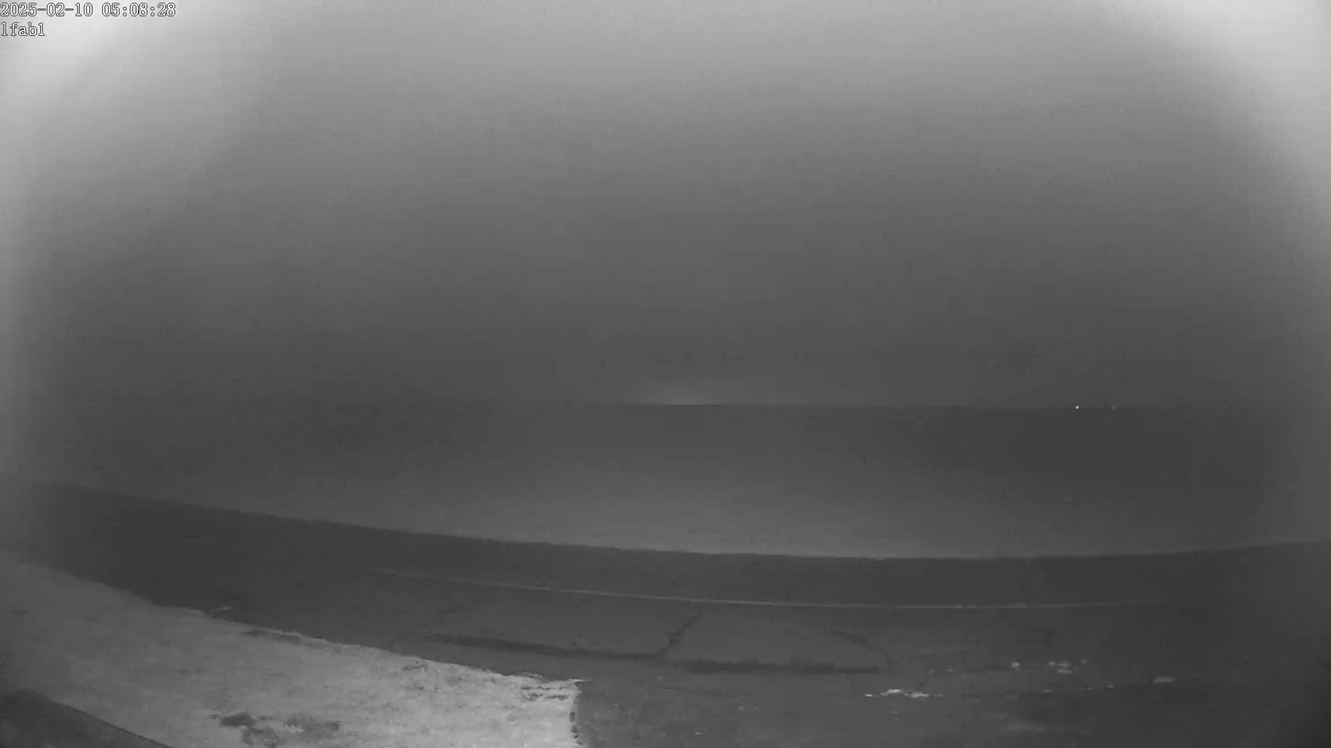 A low-visibility, foggy scene shows a dark body of water extending to a hazy horizon.