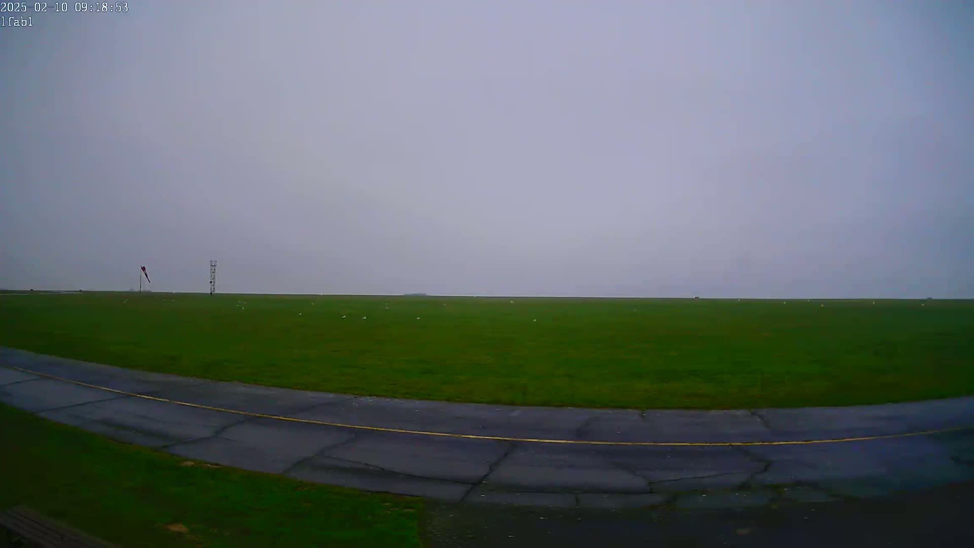 A grassy airfield with a curved tarmac taxiway is visible under an overcast sky.