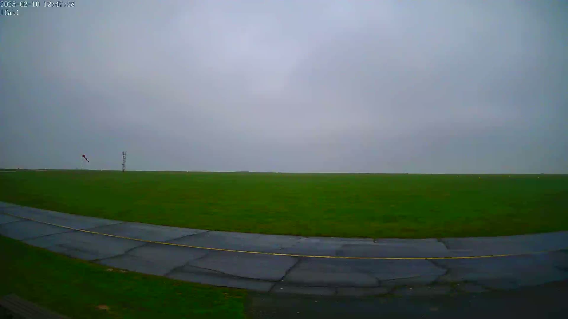 A grassy field with a paved road curving through it under an overcast sky.
