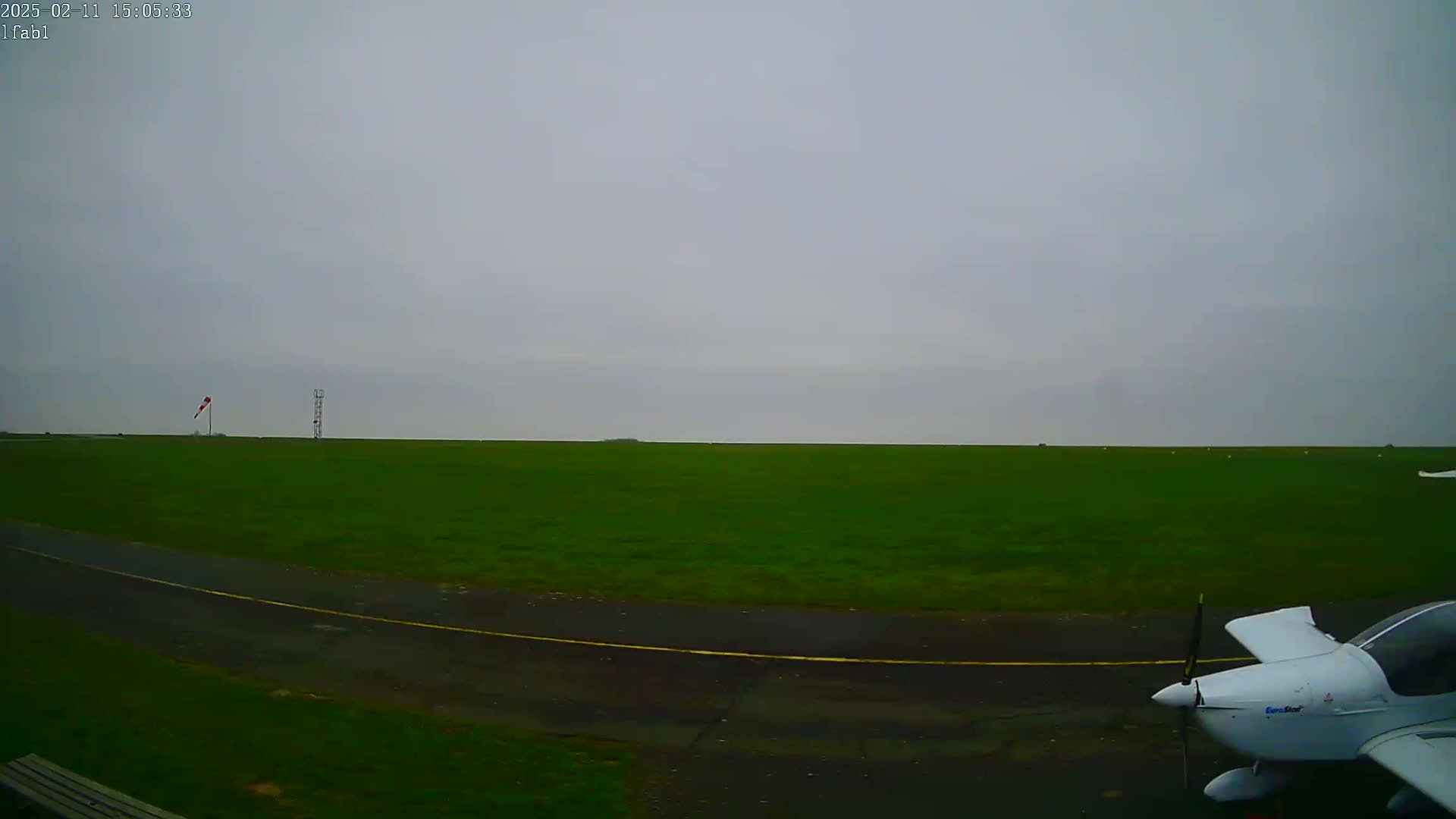 A small white airplane sits on a grassy airfield under an overcast sky.