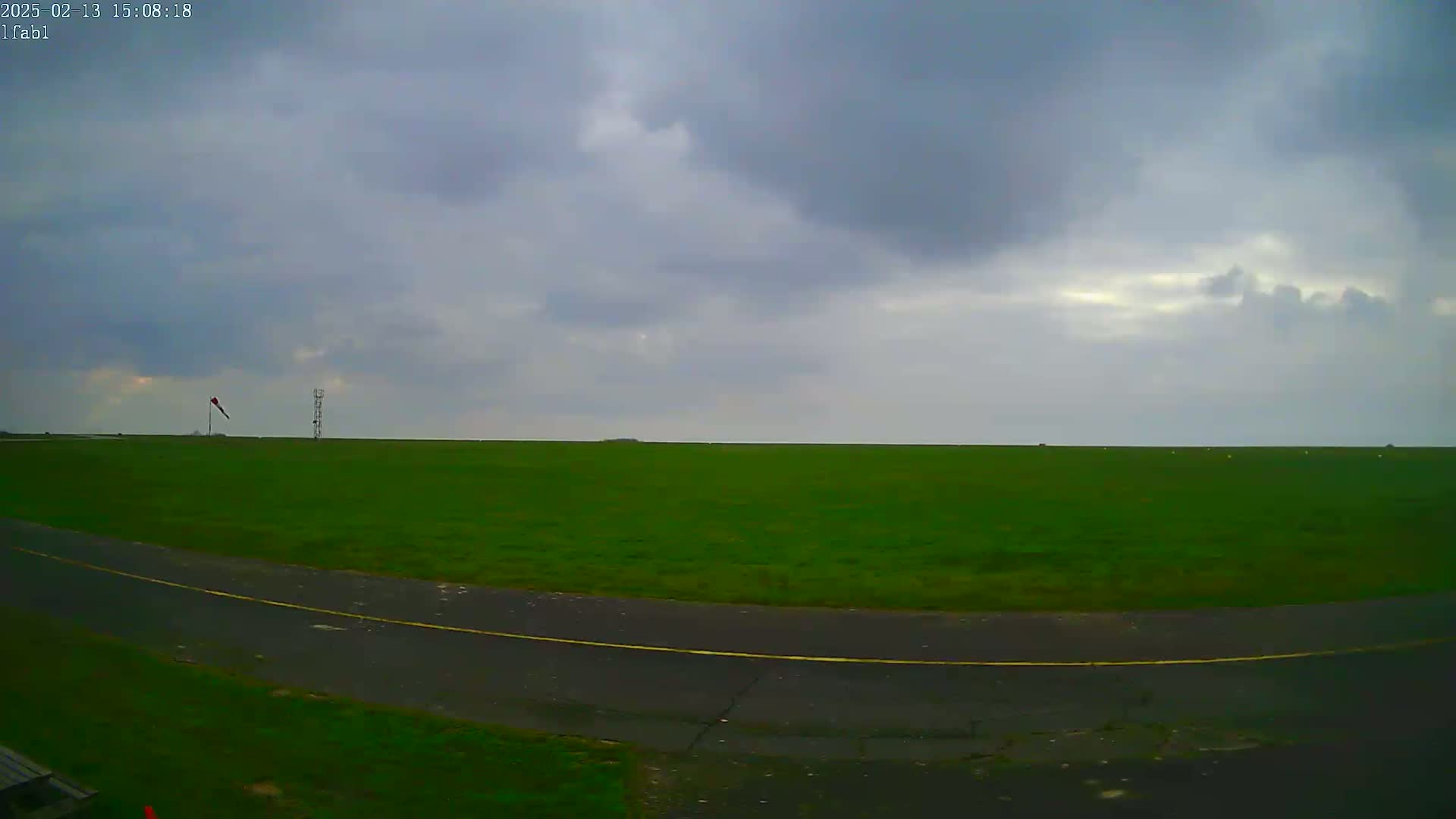 A vast green field, under an overcast sky, is bordered by a paved road with a yellow line.