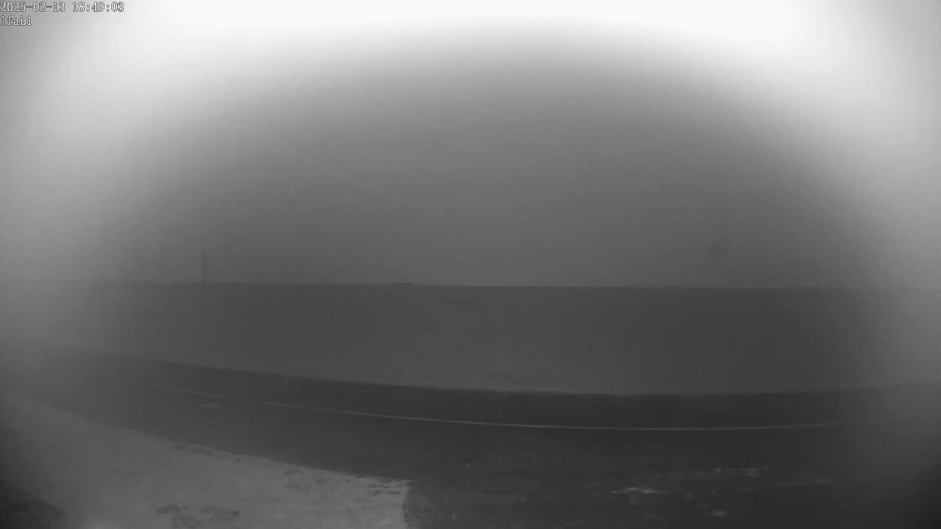A foggy, low-visibility scene shows a dark ground plane with a thin, dark line near the bottom, possibly a road or track.