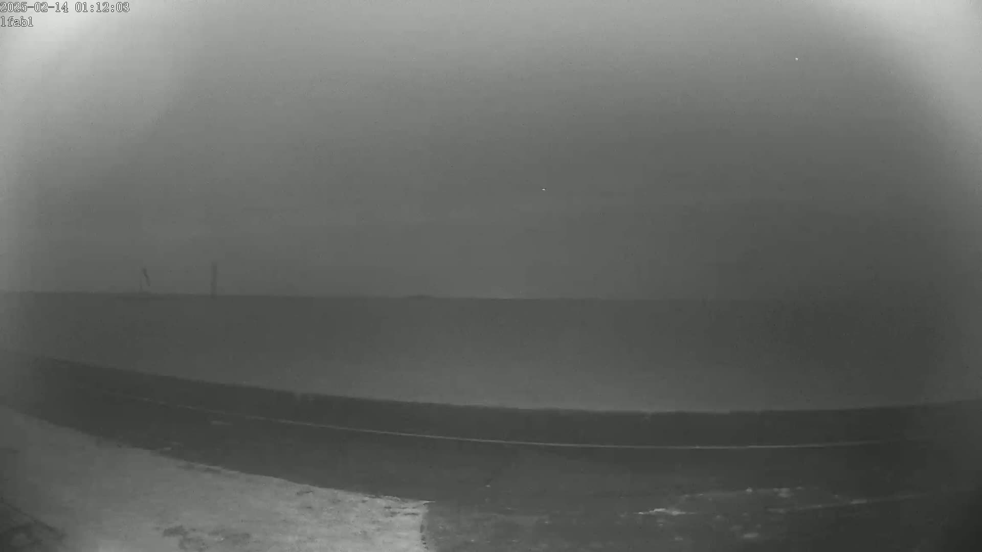 A low-light, foggy or hazy outdoor scene shows a flat expanse of land with a dark road or path in the foreground.