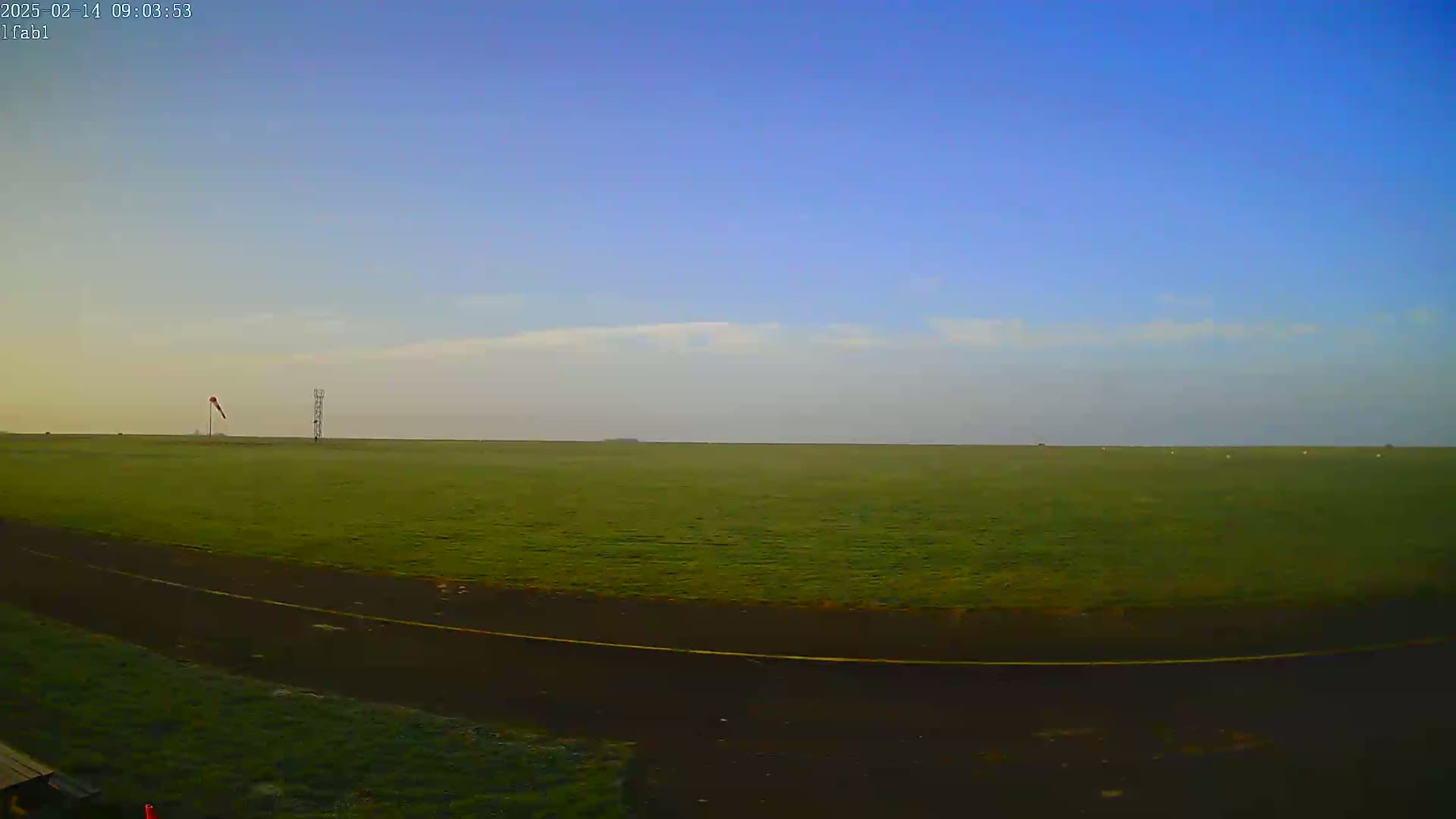 A vast, flat green field stretches to the horizon under a clear, mostly blue sky with a few wispy clouds.