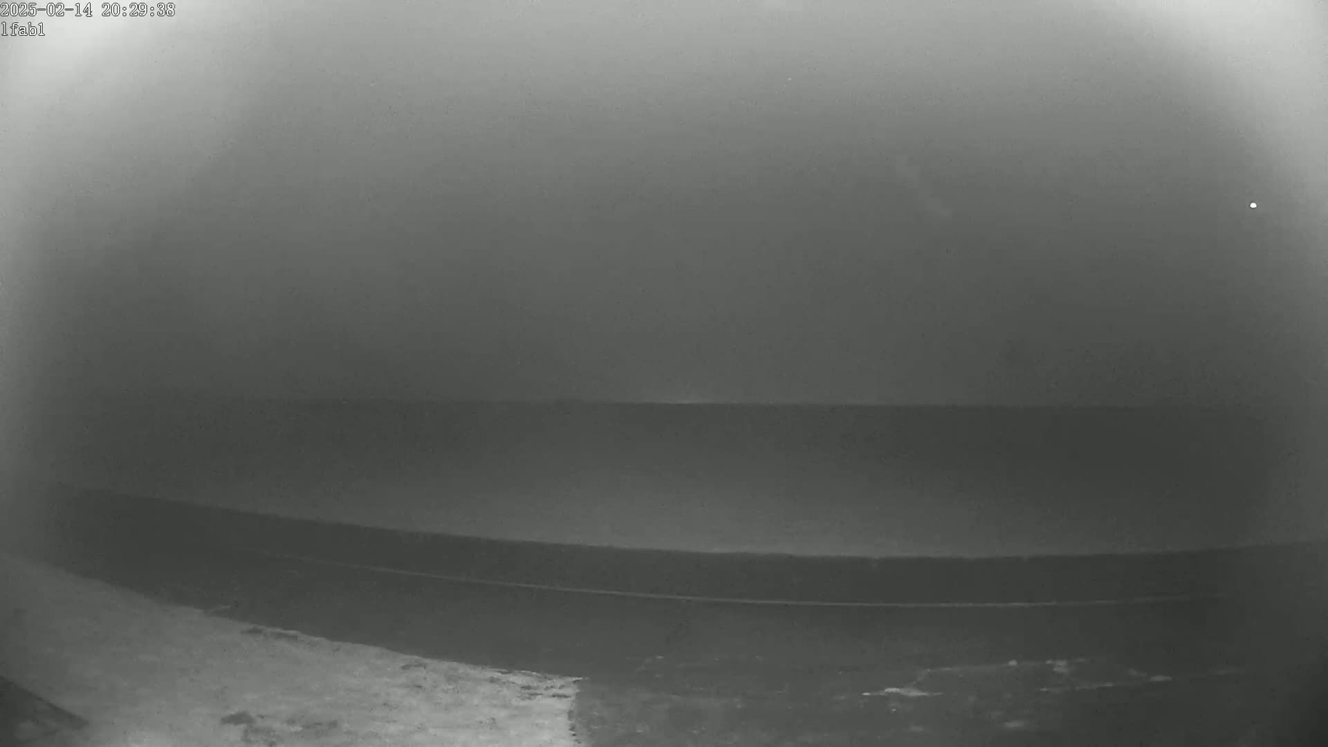 A dark, foggy, or hazy scene shows a dark body of water, possibly a lake or ocean, stretching to a hazy horizon under a dark sky.
