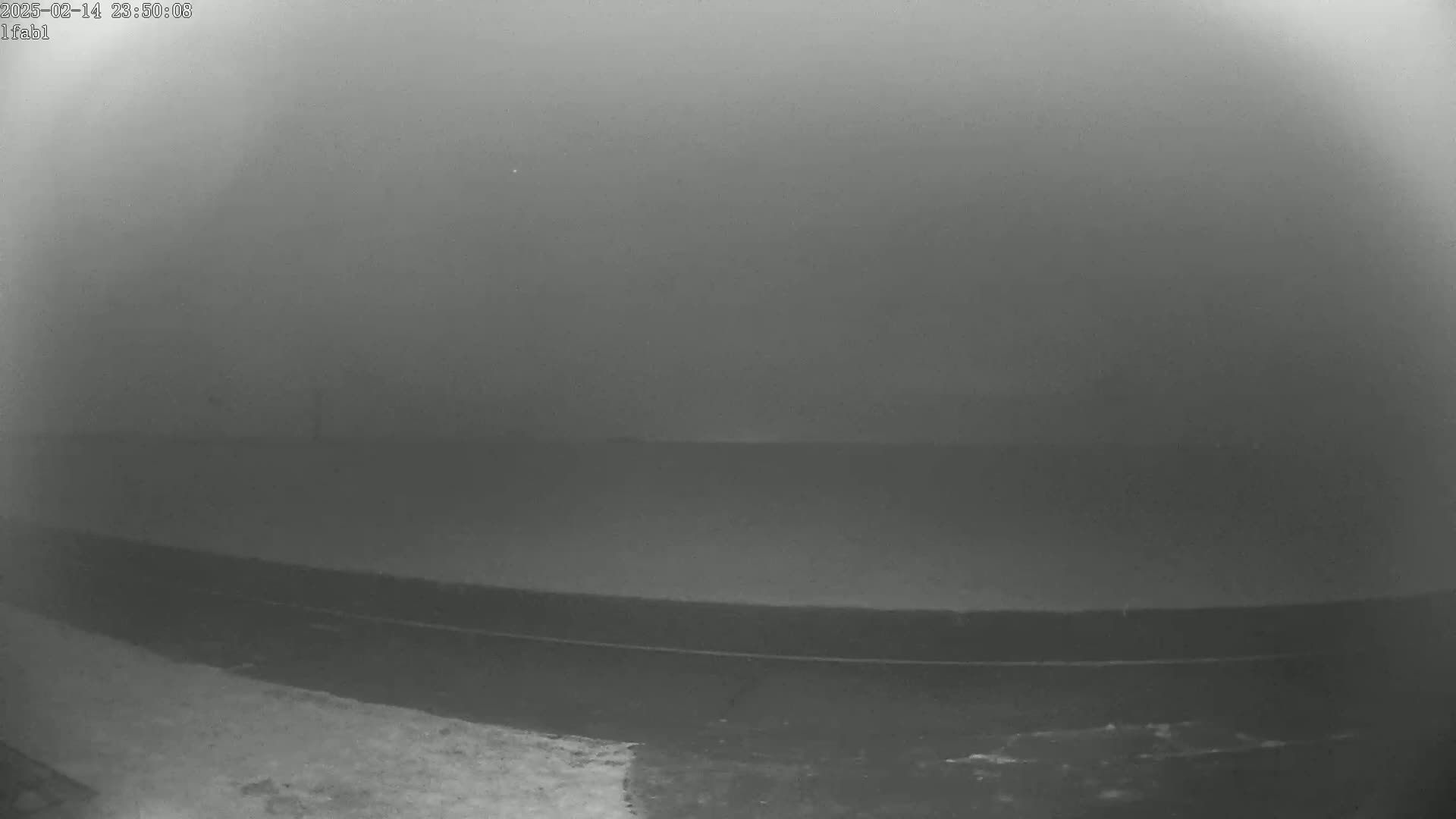 A low-visibility, foggy scene shows a dark roadway and some ground, possibly snow or ice, in the lower left corner.