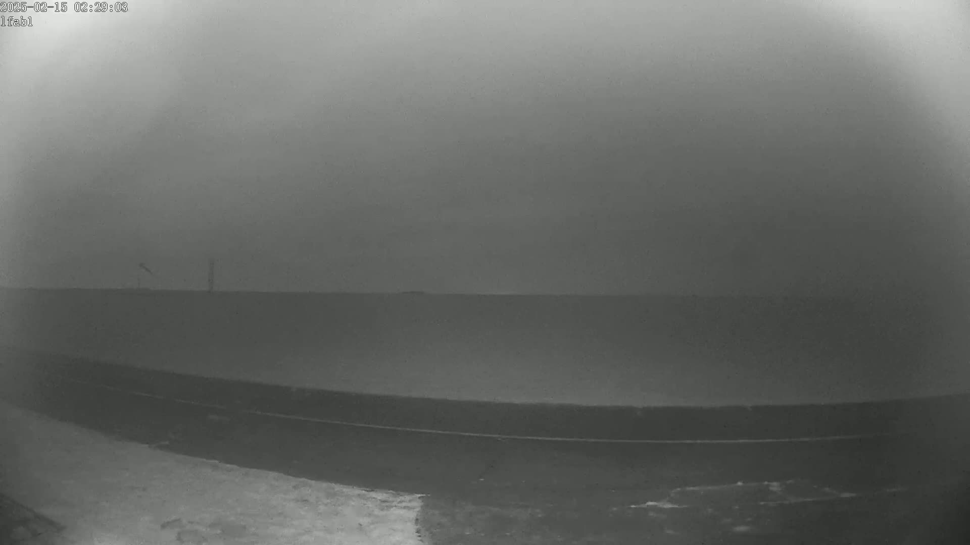 A low-visibility, overcast scene shows a flat, dark landscape with a road and some snow in the foreground.