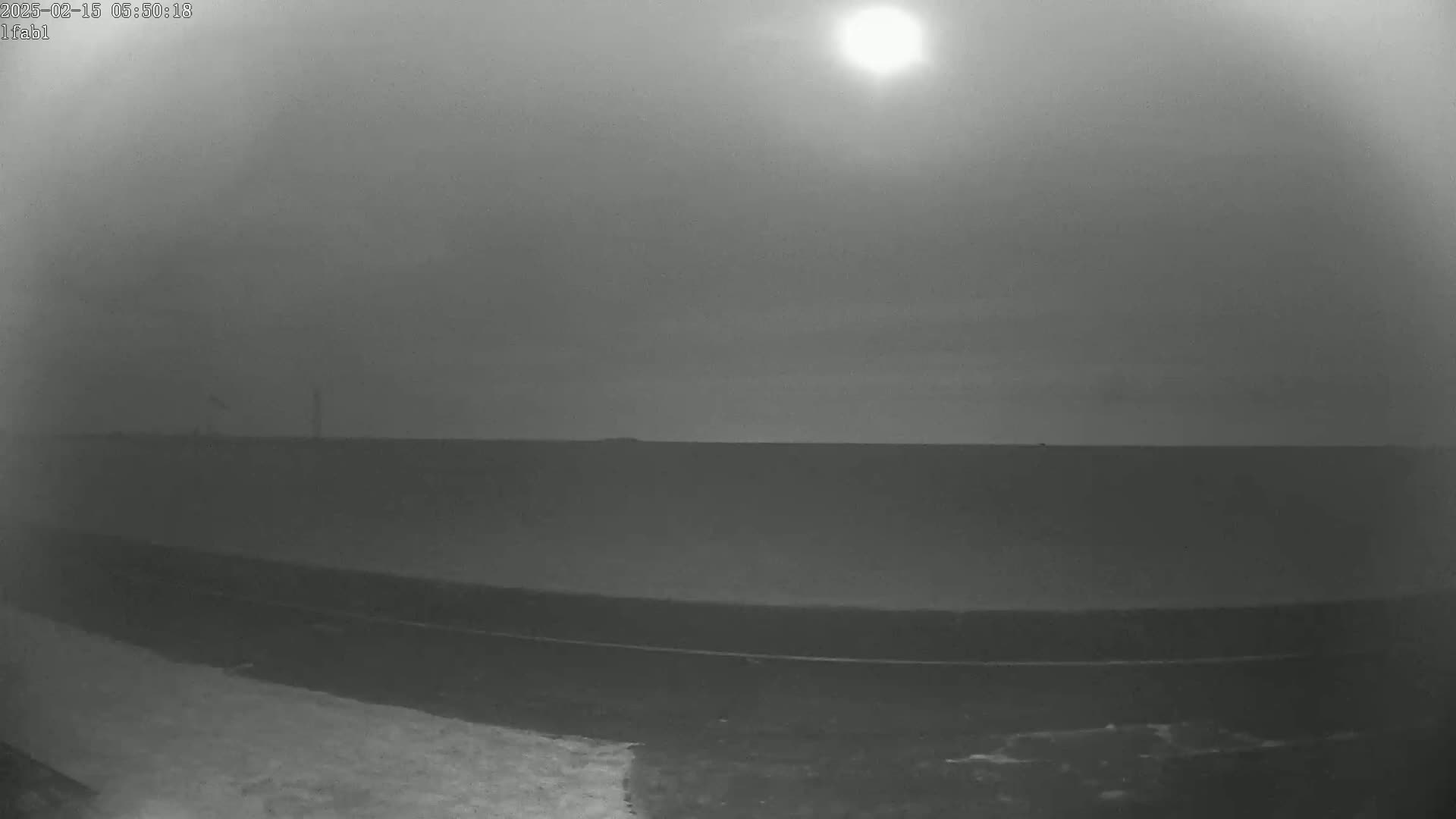 A hazy, bright sun shines over a flat, dark landscape with a thin, dark line in the foreground, possibly a road.
