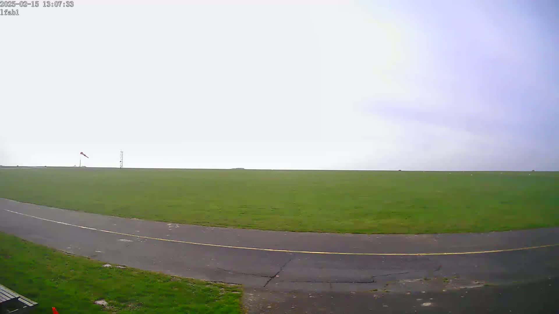 A grassy field with a paved roadway curving through it is visible under an overcast sky.