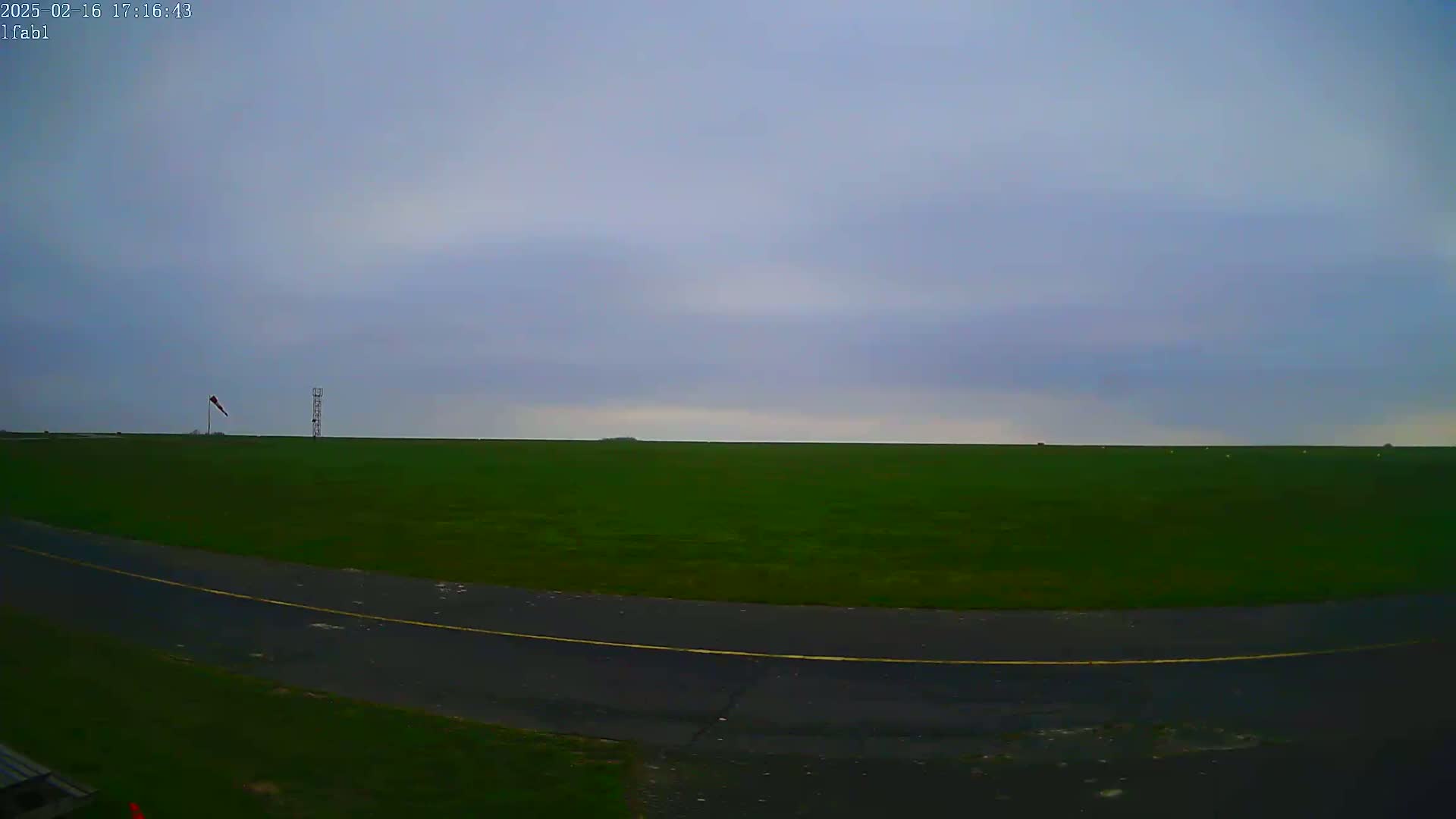 A flat, green field under a cloudy sky is partially visible beyond a paved area with a yellow line.
