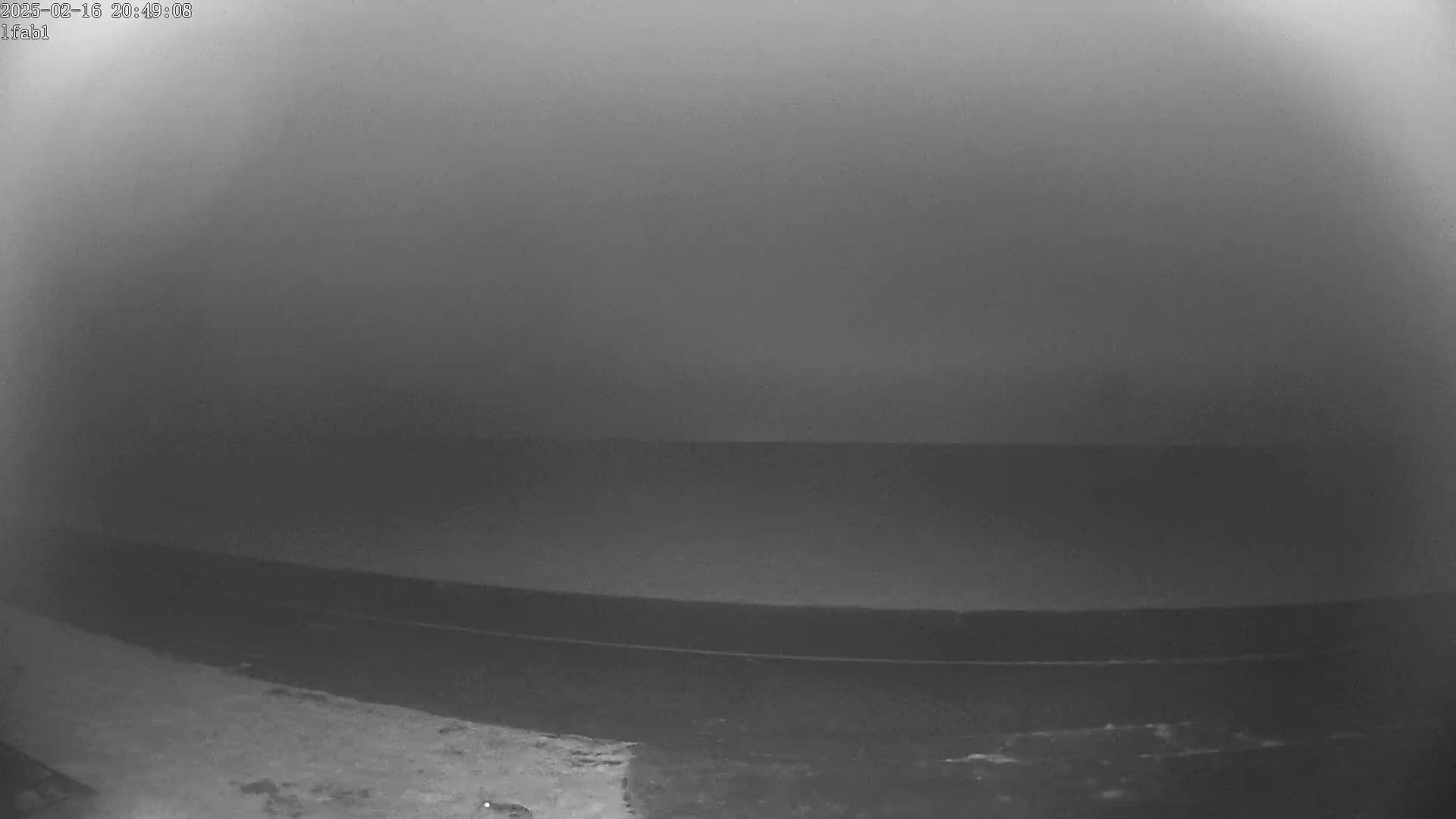 A low-light, possibly nighttime, image shows a dark gray expanse of water under a hazy or foggy sky.