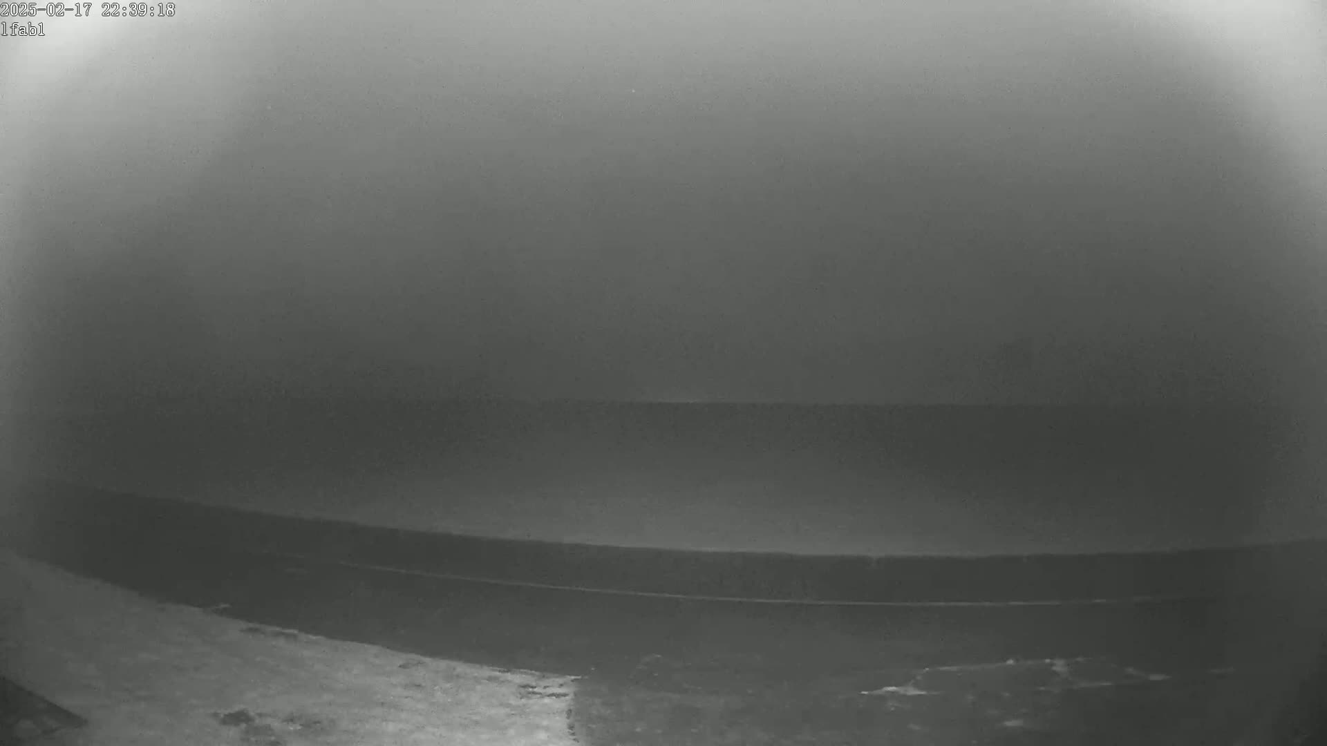 A low-light, possibly nighttime, view shows a dark, flat expanse of water under a foggy or hazy sky.