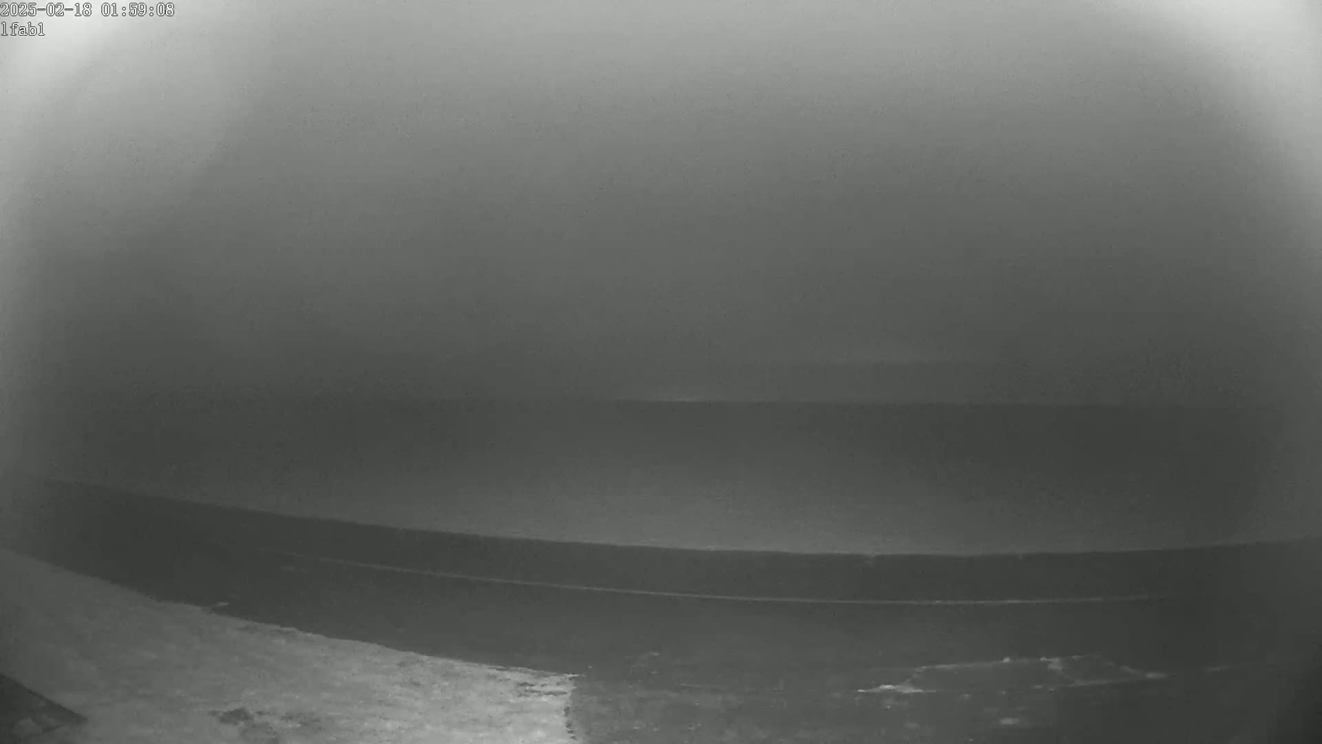 A dark, foggy scene shows a body of water with a dark shoreline.