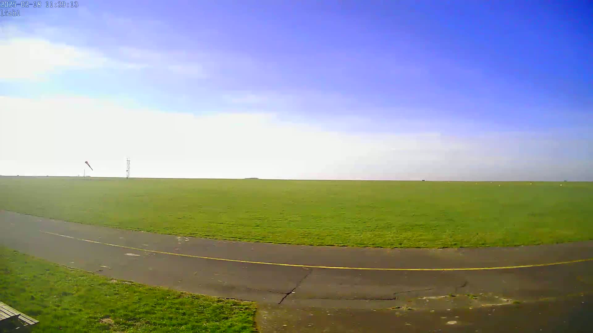 A paved path curves through a large expanse of green grass under a mostly clear, bright blue sky.