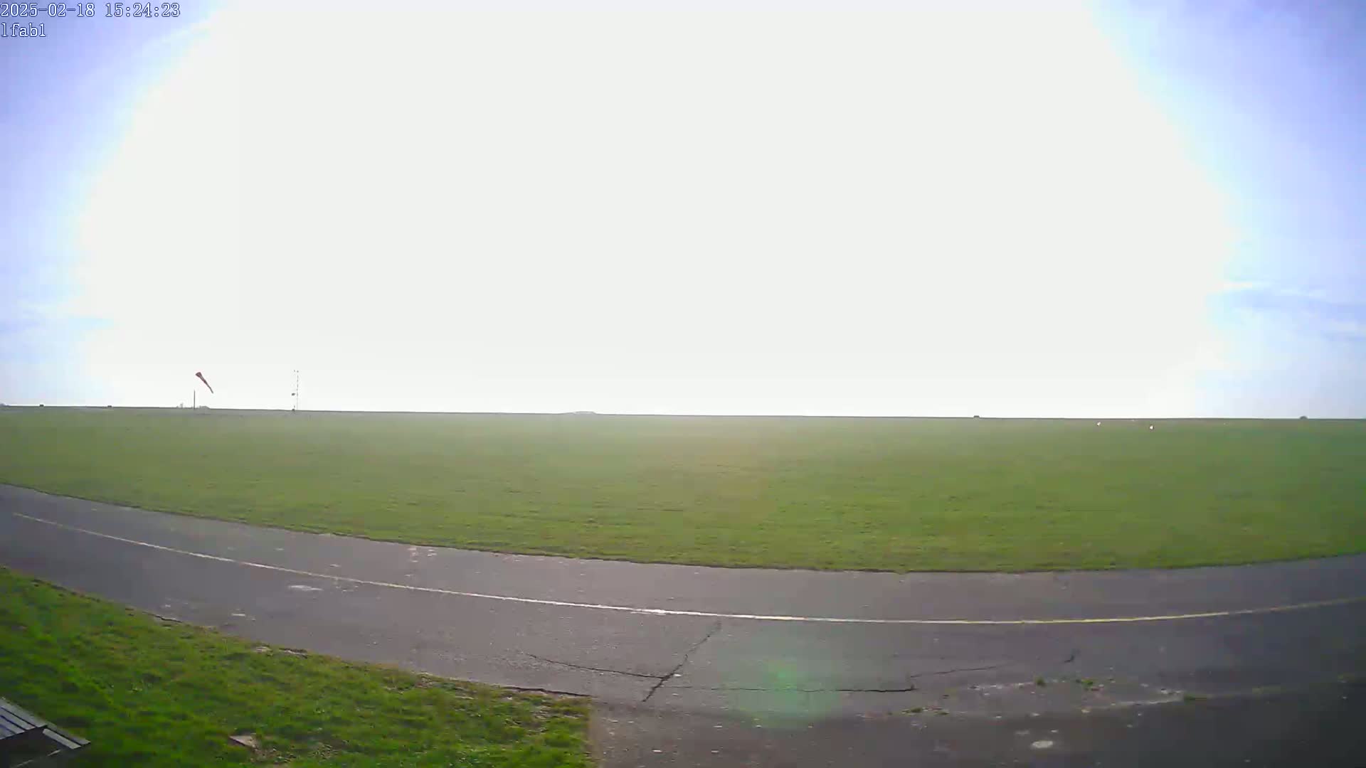 A paved path curves through a large grassy field under a mostly cloudy sky.