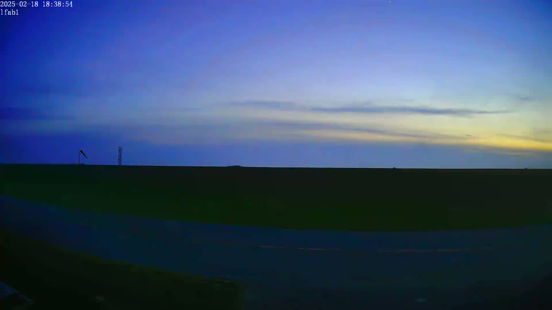 A flat, dark landscape is visible under a twilight sky with thin, light clouds.