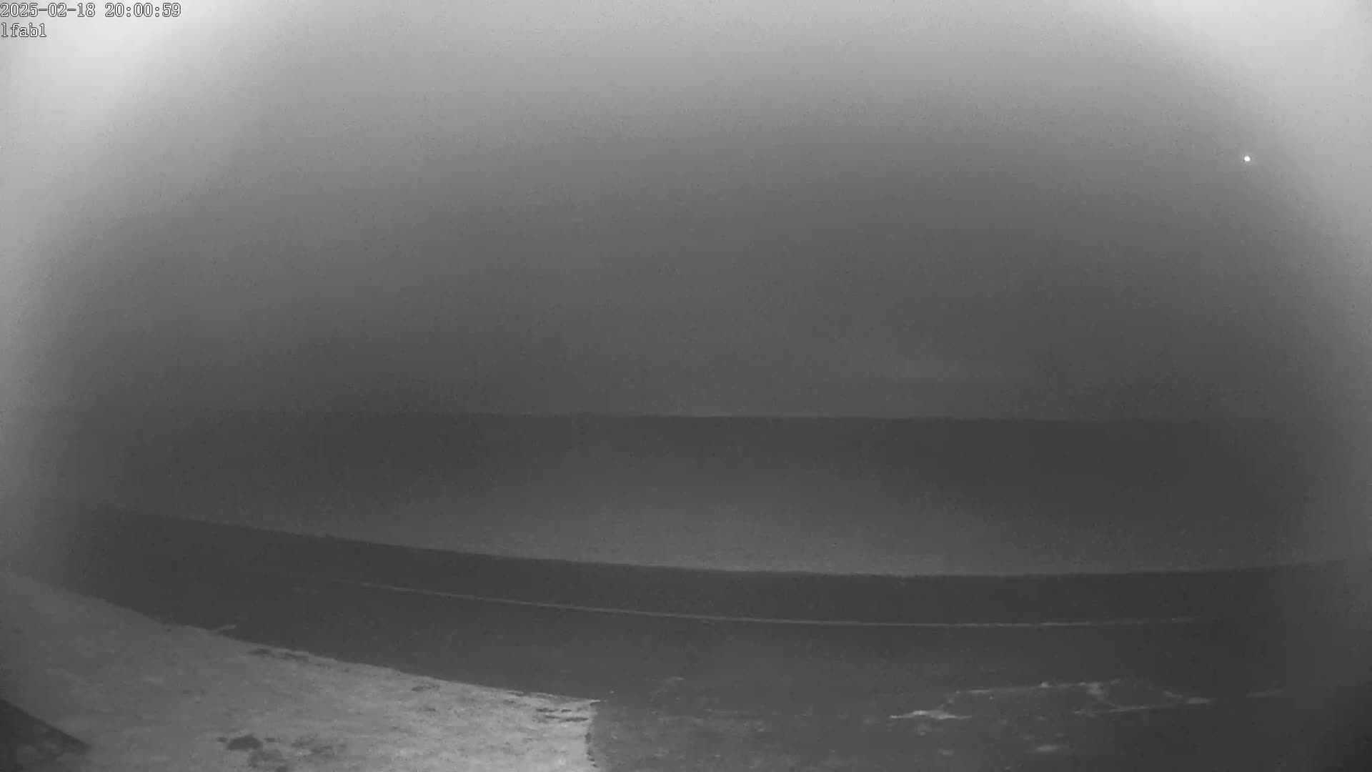 A dark, foggy scene shows a flat expanse of land with a road, possibly near a body of water, under a night sky with a single bright light visible.