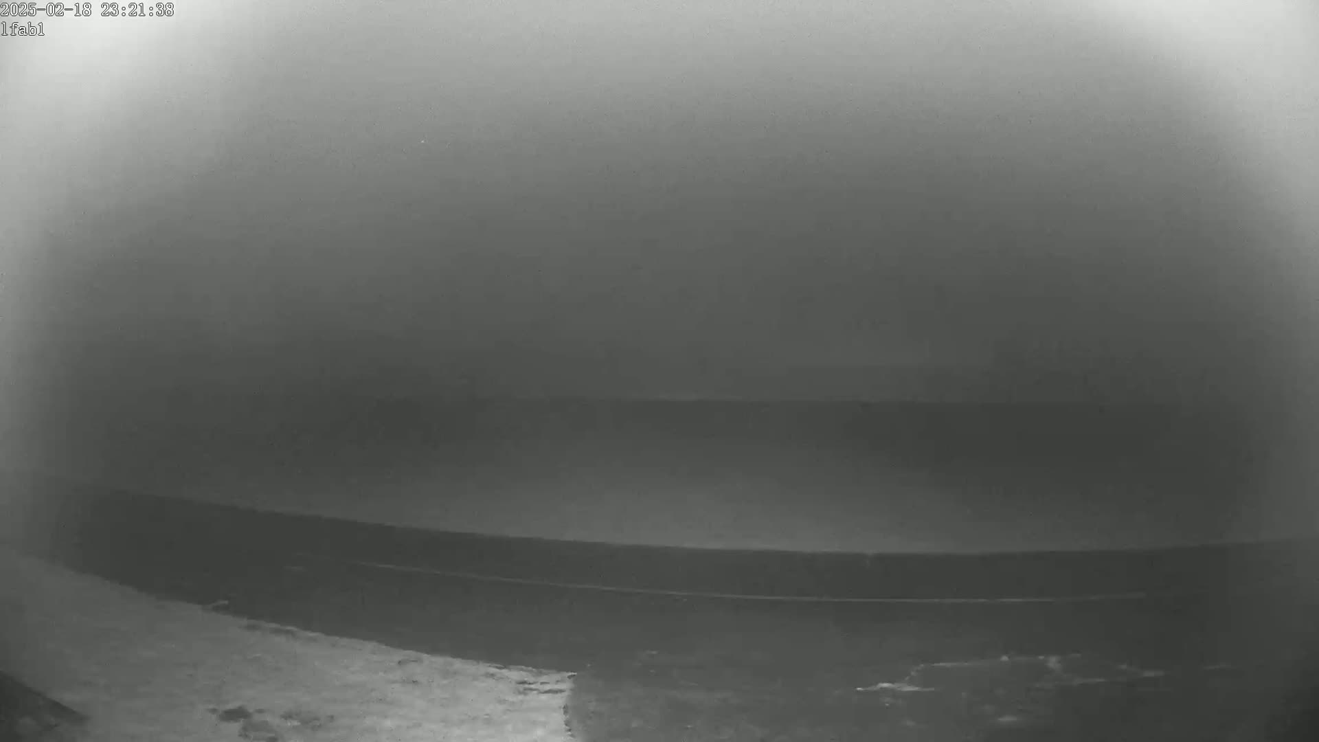 A low-light, blurry image shows a dark, possibly flat, surface extending to a hazy horizon under a foggy or overcast sky.