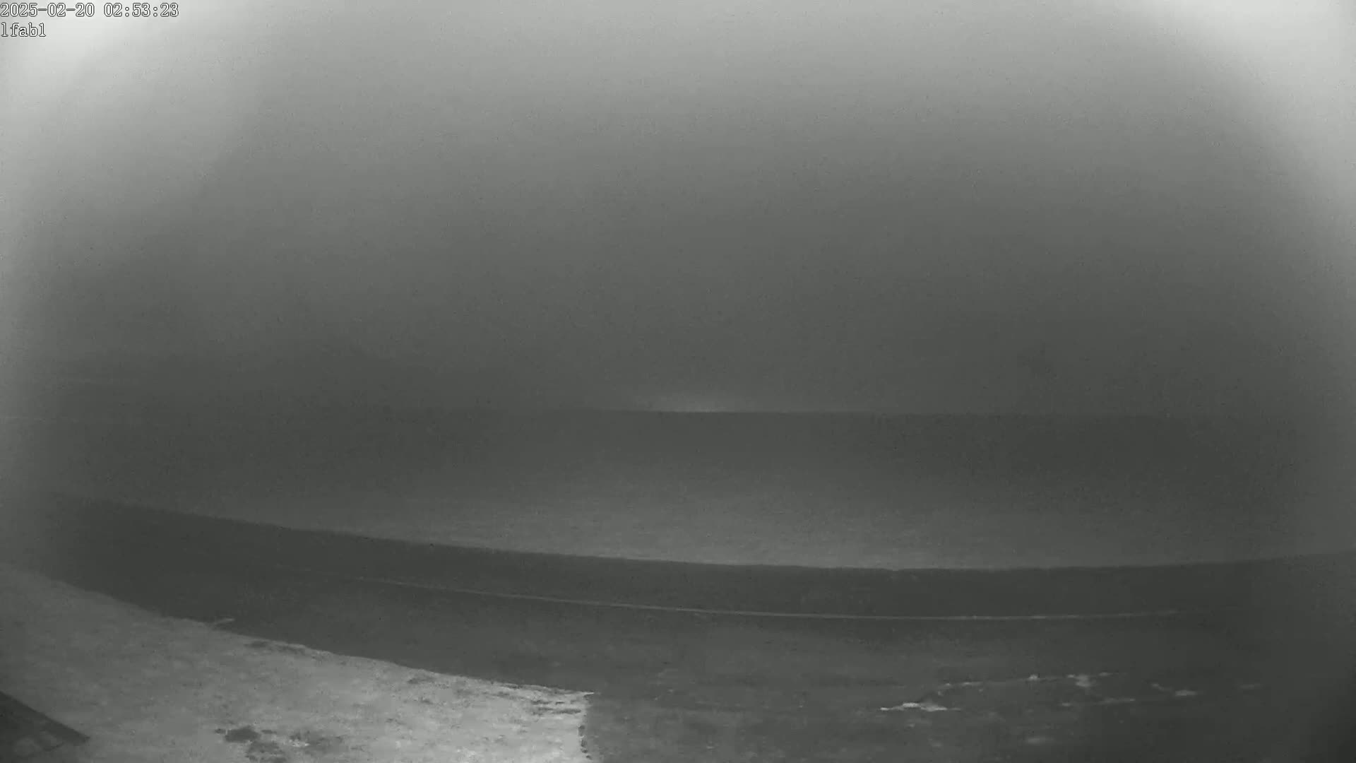 A foggy, dark scene shows a flat, dark expanse of land with a faint line suggesting a road or path in the foreground.