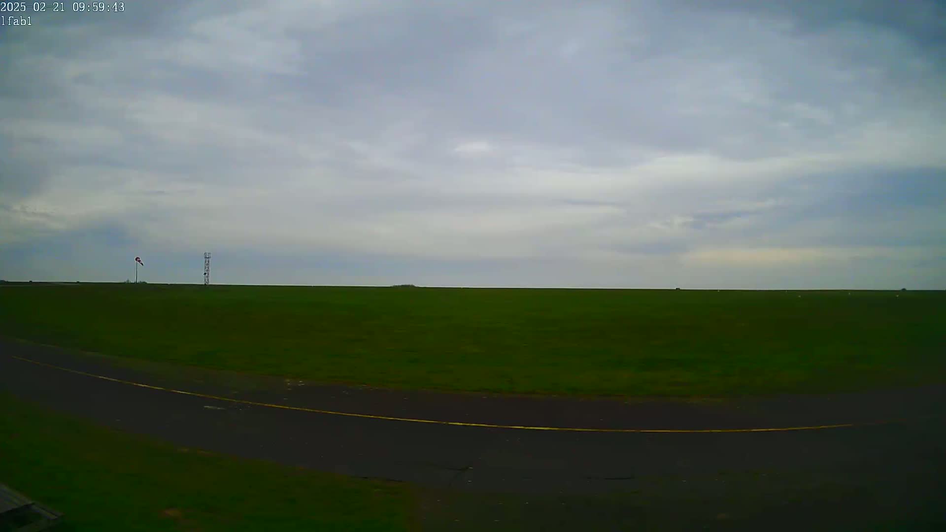 A wide, flat expanse of green grass under a cloudy sky is bisected by a dark asphalt roadway with a yellow line.