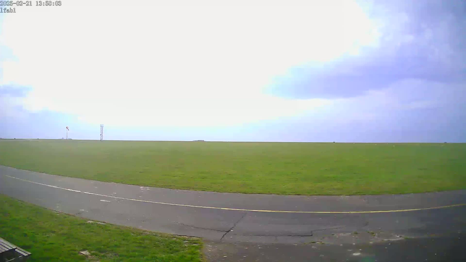 A paved path curves through a large, grassy field under a mostly cloudy sky.