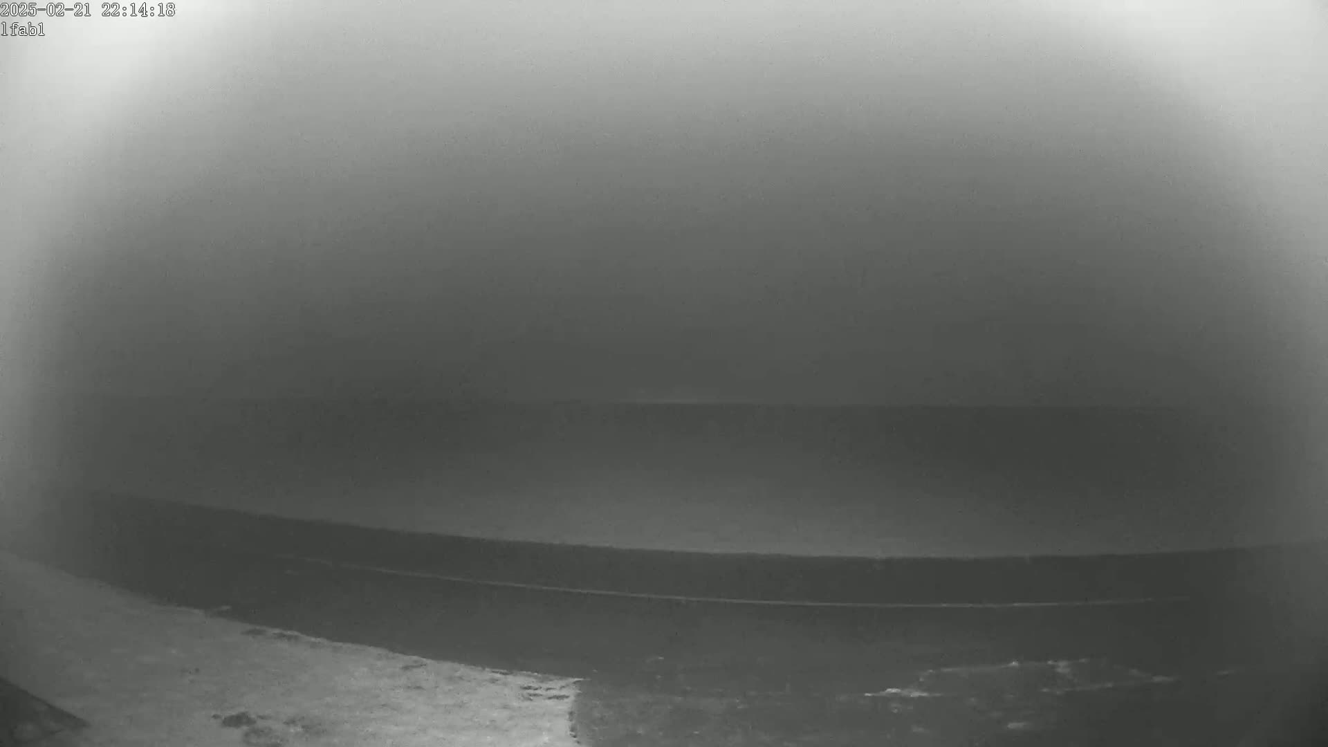 A low-visibility, foggy scene shows a dark, flat expanse of water, possibly a body of water or a dock, with a slightly lighter area in the foreground.