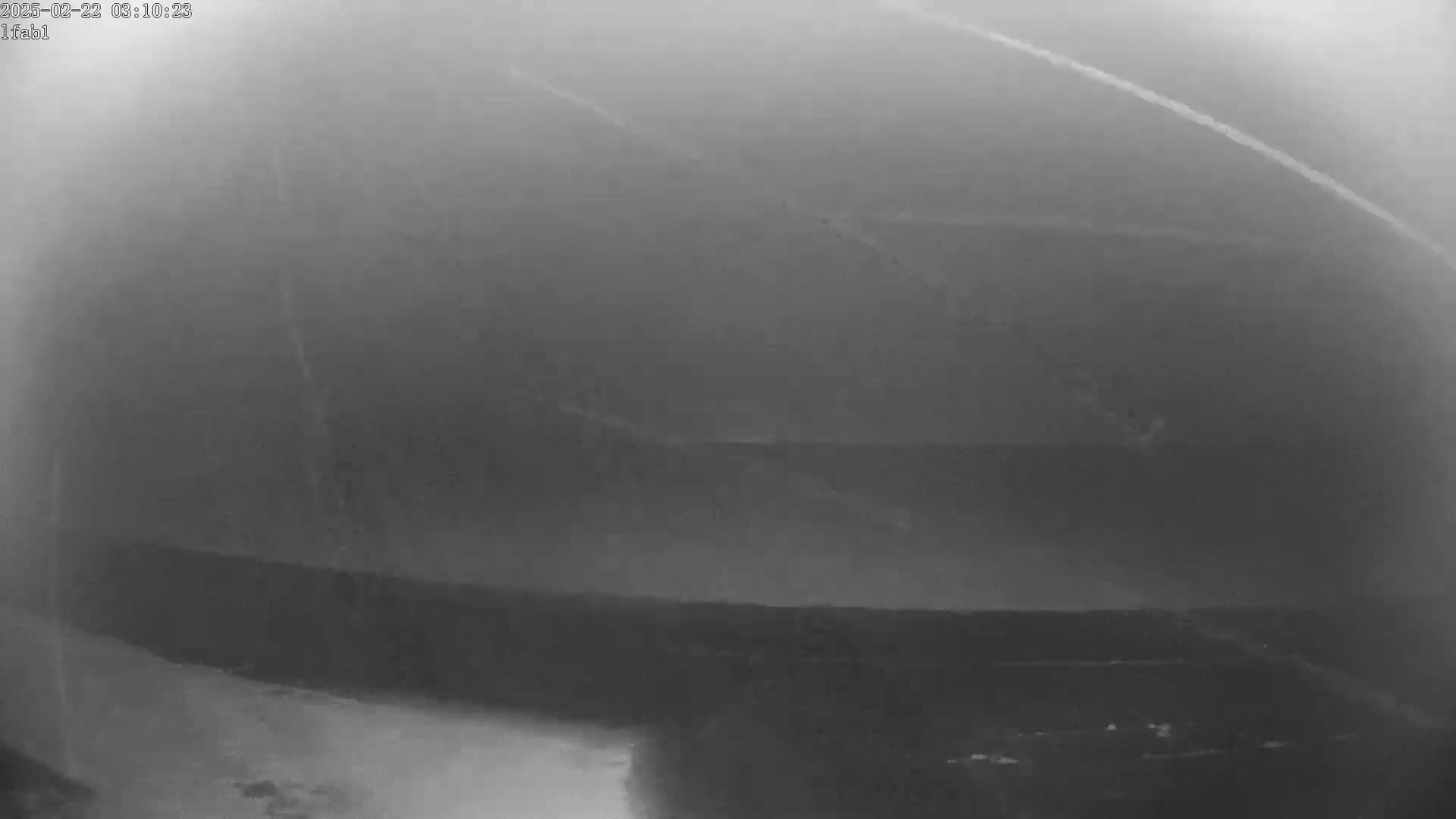 A blurry, grayscale image shows a dark, possibly mountainous landscape under foggy or hazy conditions.