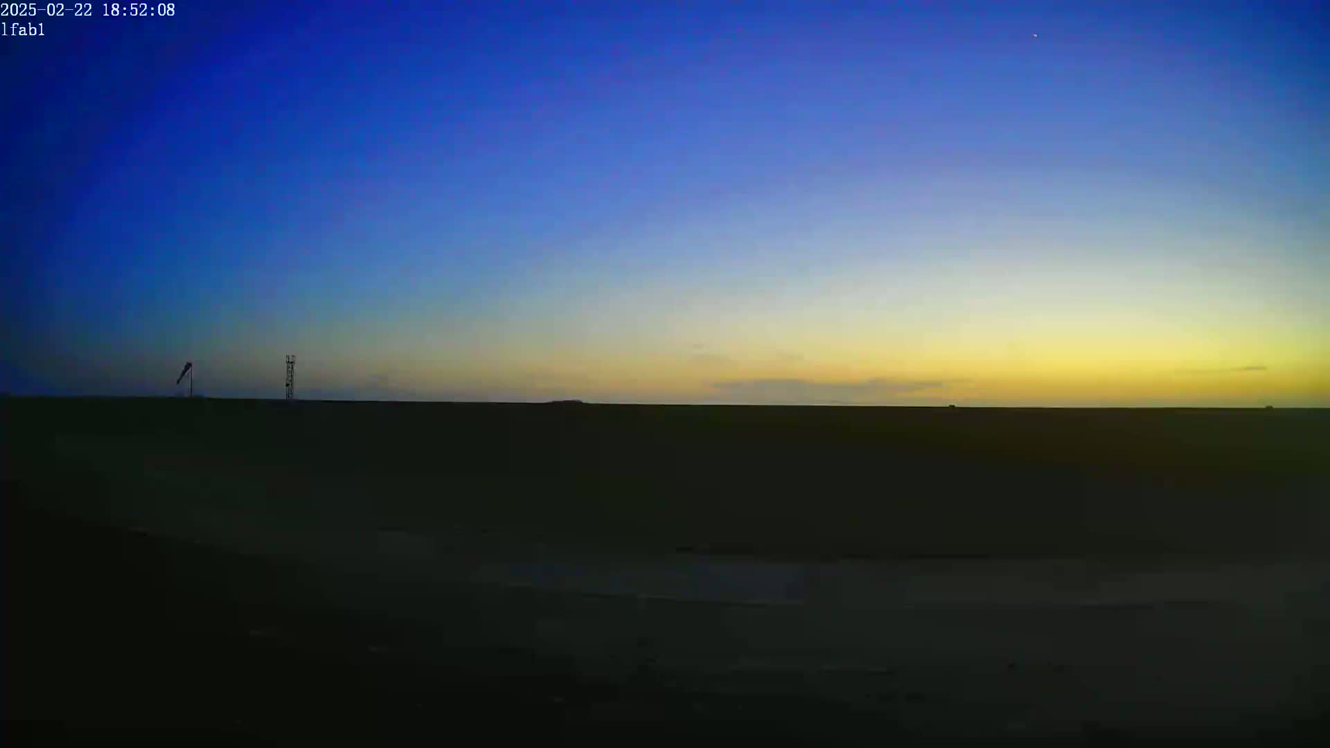 A flat, dark landscape is silhouetted against a twilight sky transitioning from deep blue to yellow at the horizon.