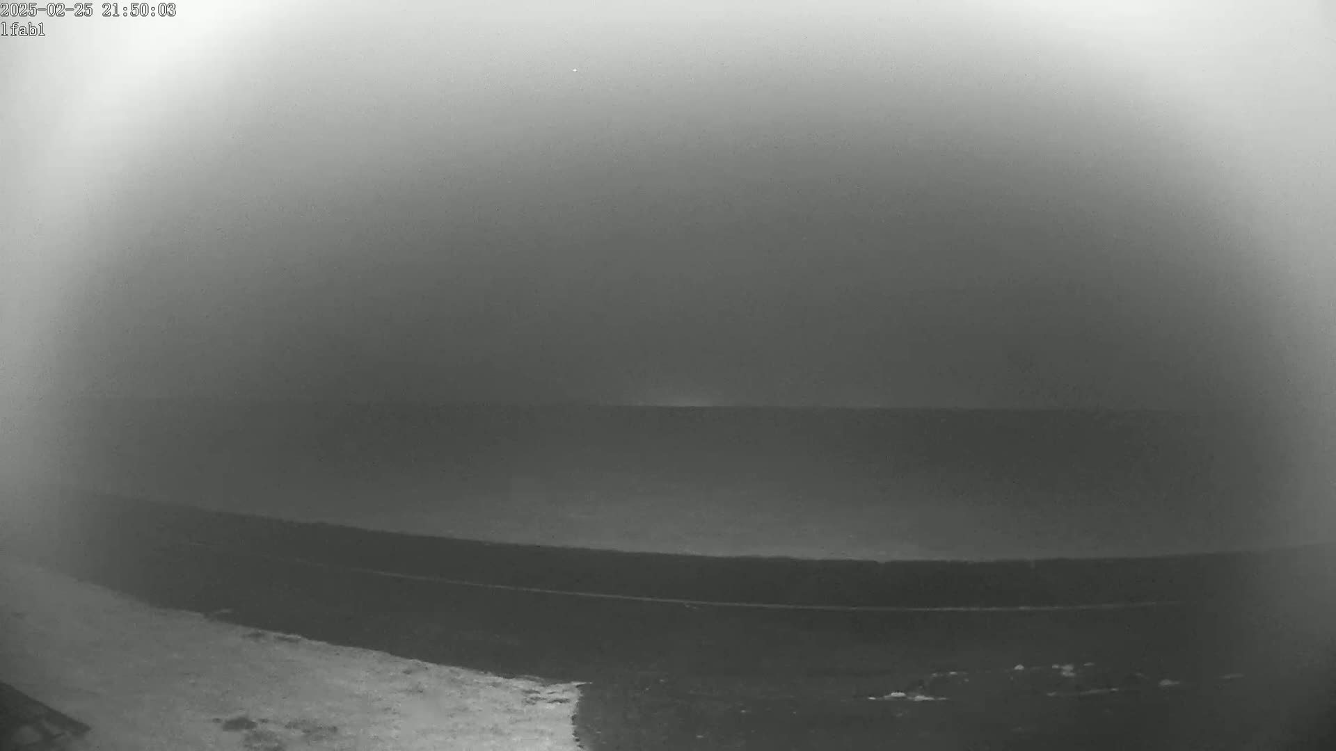 A dark, foggy landscape shows a flat, dark expanse of land or water meeting a dark sky.