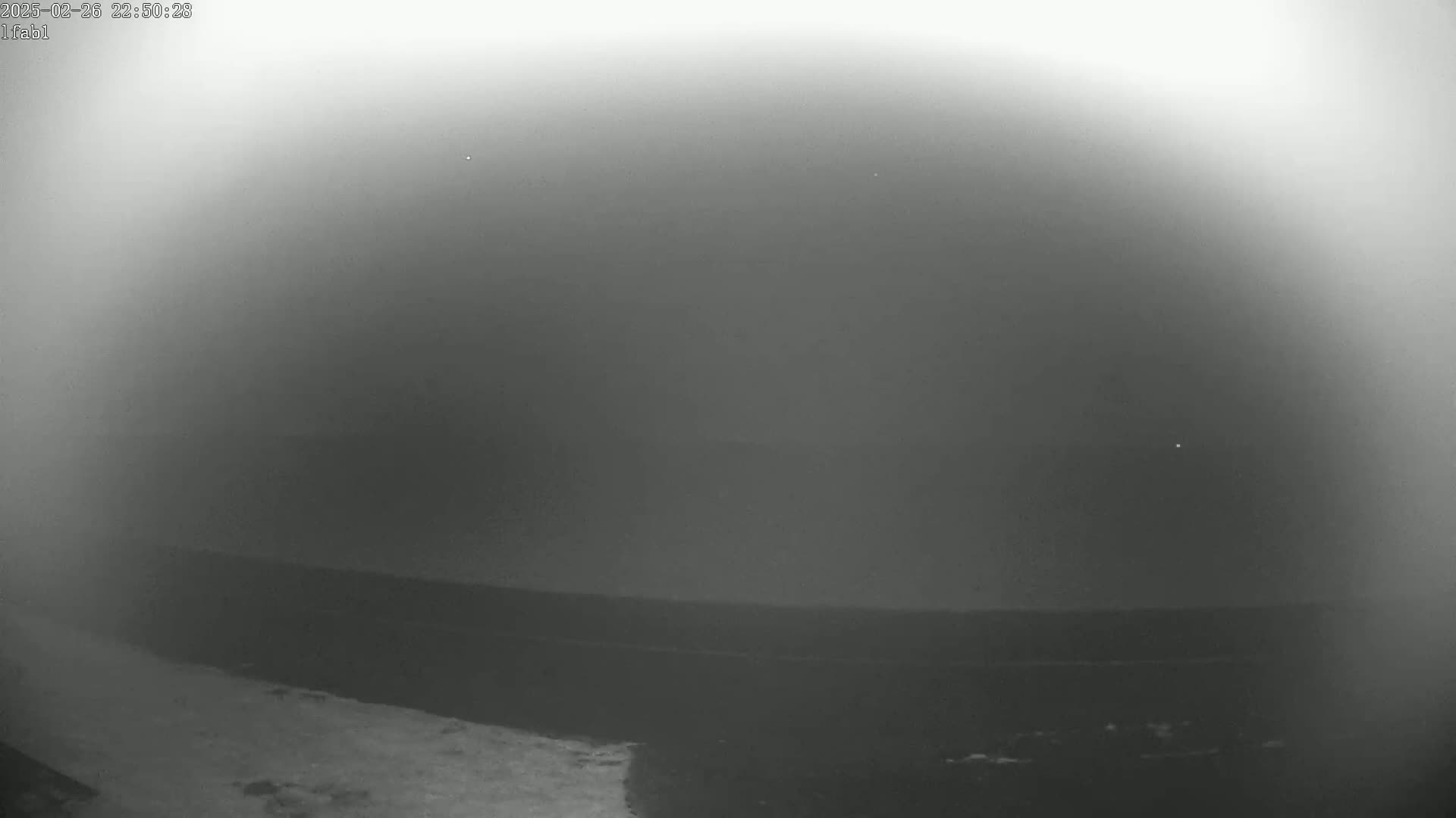 A hazy, dark gray nighttime scene shows a flat, dark landscape with a brighter area in the bottom left corner.