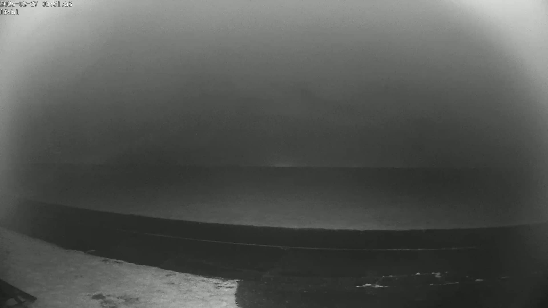 A dark, foggy scene shows a flat, dark surface, possibly a deck or road, leading to a foggy horizon.