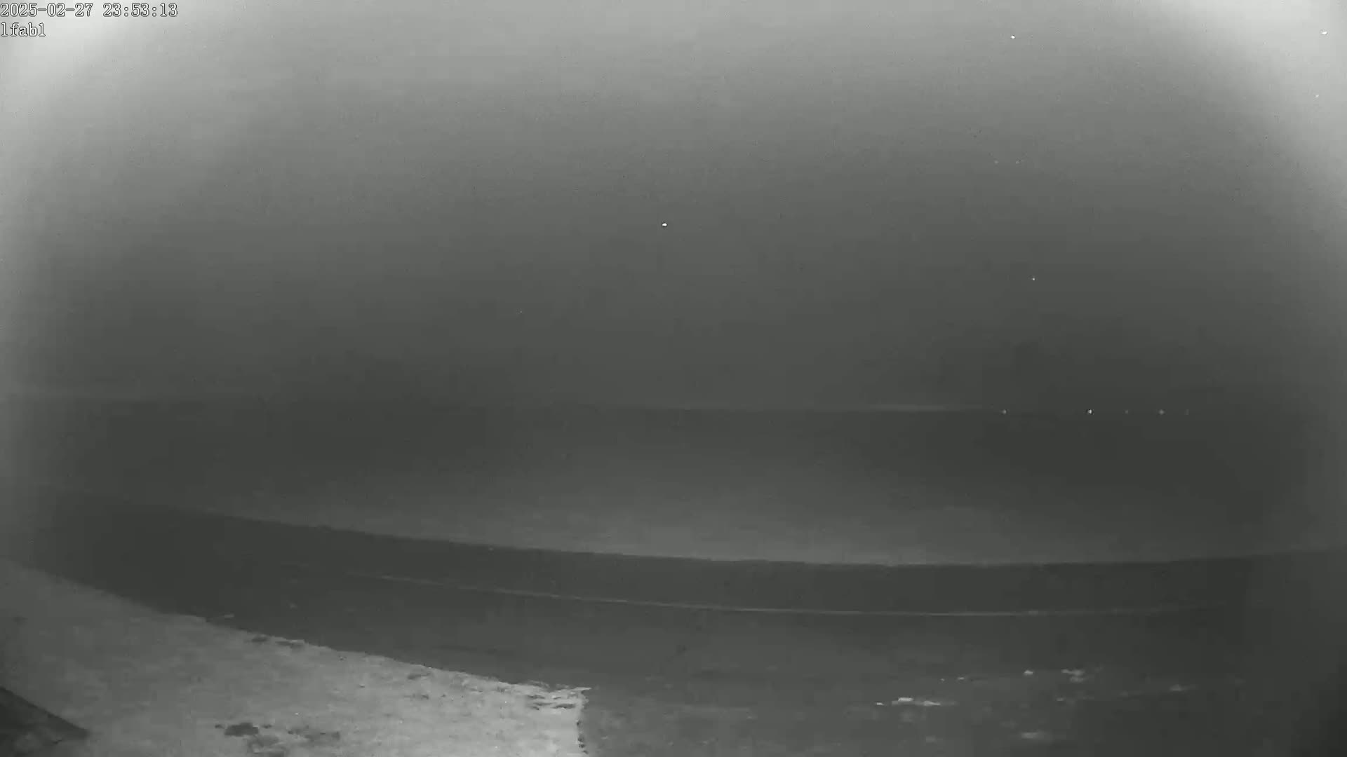 A low-light nighttime image shows a dark, flat expanse of land or water under an overcast sky.