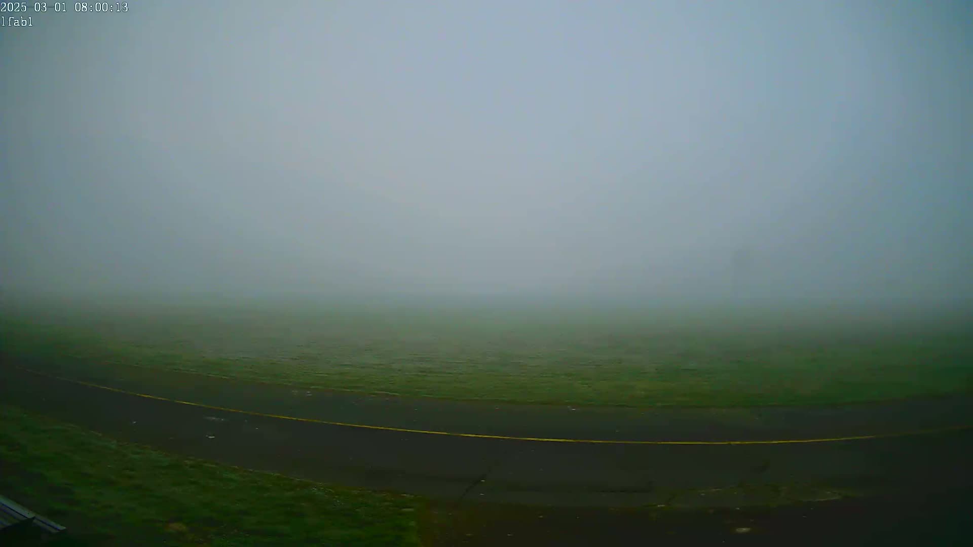 A thick fog obscures a grassy field and a paved road with a yellow line.